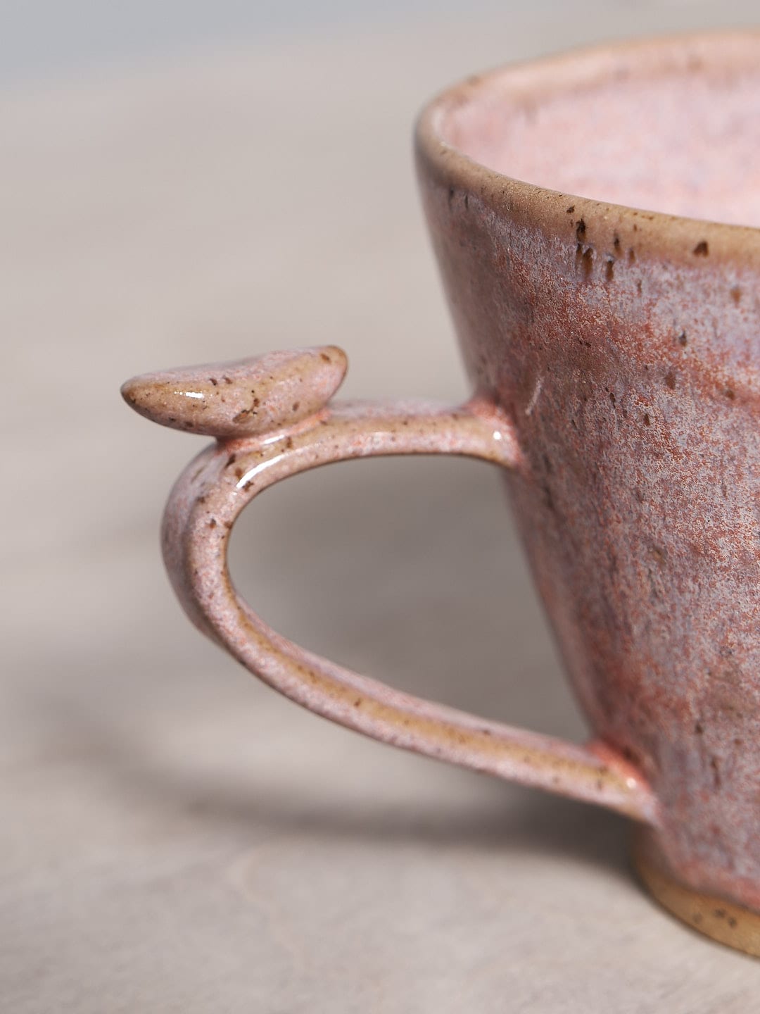 A Jino Ceramic Studio Bird Handle Mug - Rhubarb pink mug with a bird handle on a table.