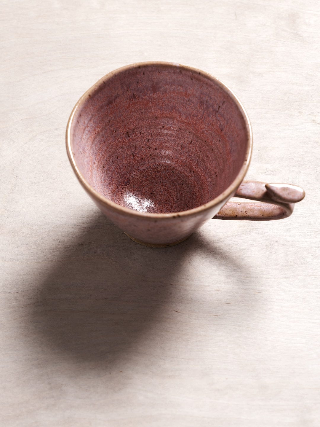 A Bird Handle Mug – Rhubarb sitting on top of a wooden table from Jino Ceramic Studio.
