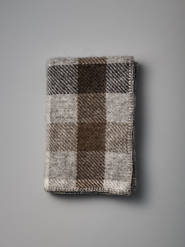 A Gotland Wool Baby Throw – Multi Grey, featuring a classic brown, gray, and beige plaid pattern inspired by timeless Klippan of Sweden designs, is displayed on a plain gray surface.