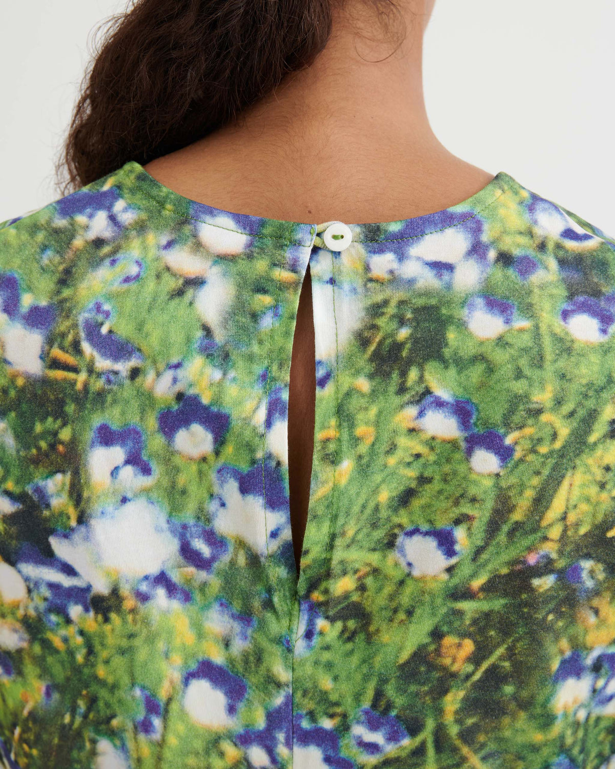 Close-up of the back of a person’s neck wearing a floral-patterned top with a small keyhole opening and a white button closure.
