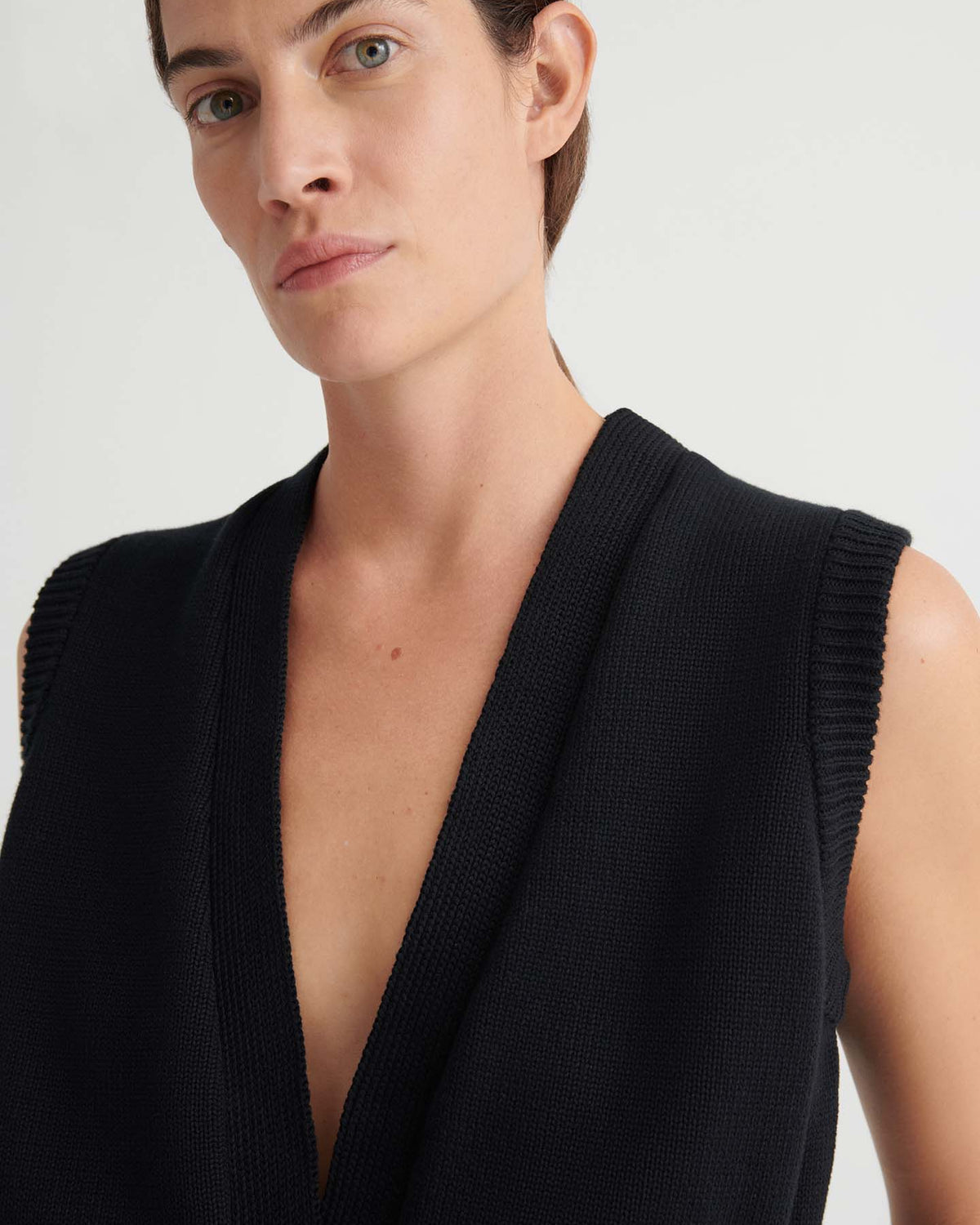 A person with short brown hair wears the Elworthy Vest – Black, a sleeveless relaxed-fit knitwear piece, and looks at the camera against a plain light background.