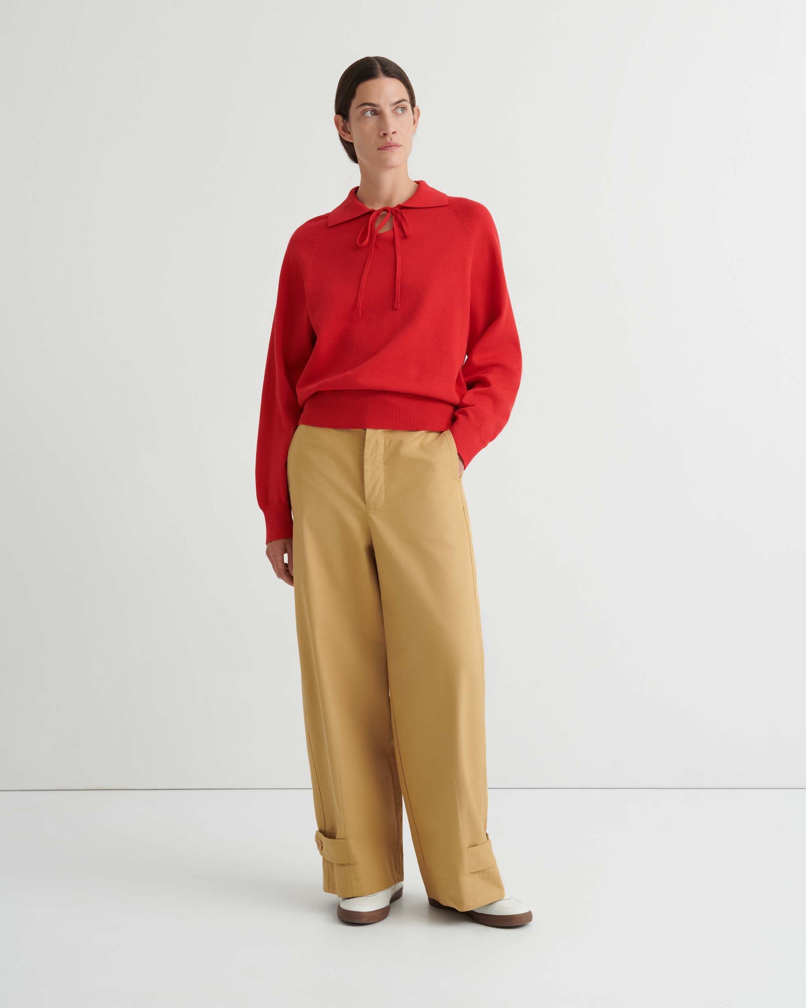 A person wearing the Keyhole Jumper in Poppy Red—a relaxed fit, long-sleeve hoodie with drawstrings—paired with tan pants, stands against a plain white background.
