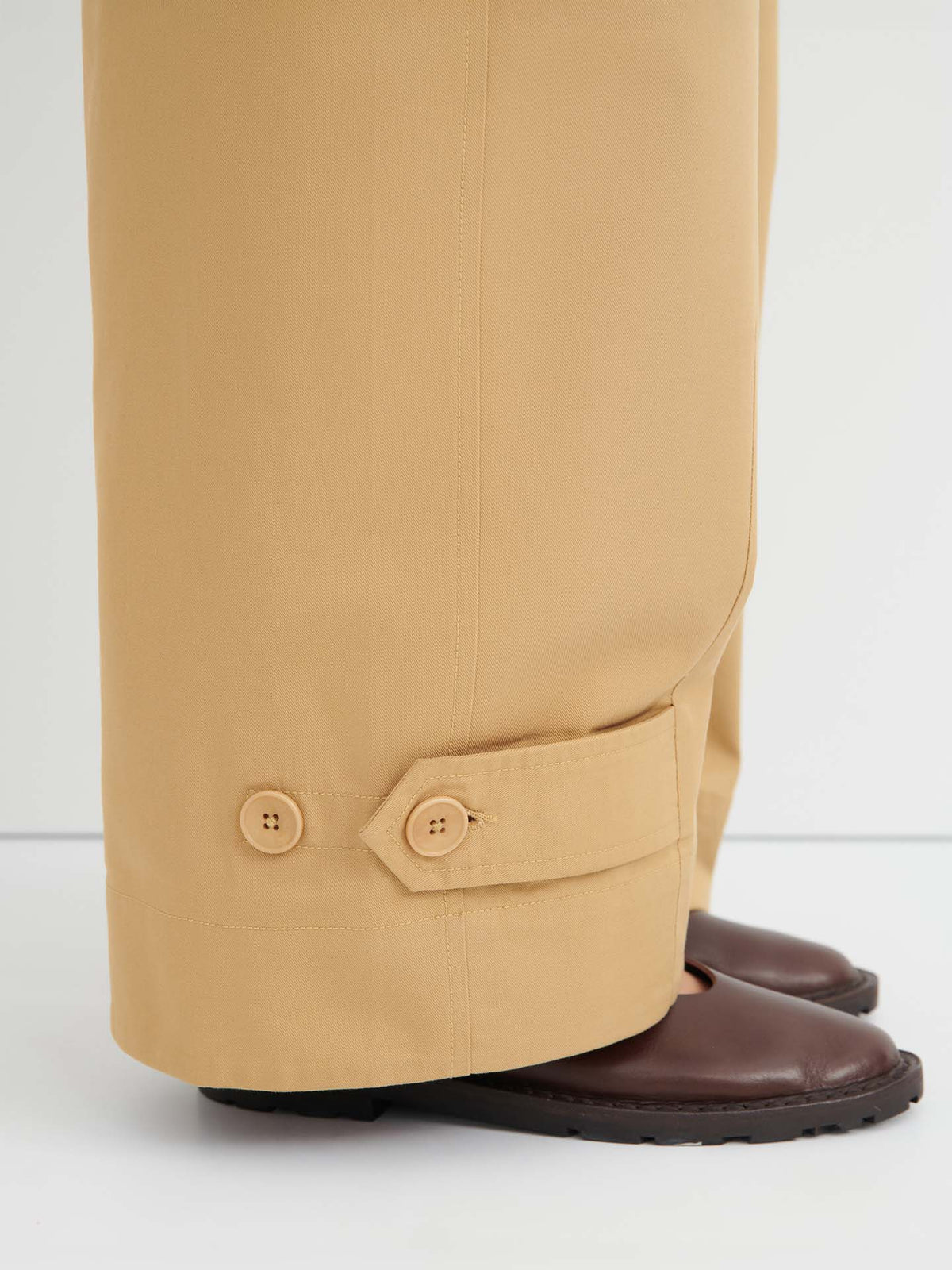 Close-up of the Tab Trouser – Driftwood, wide-leg pants with button details near the hem, featuring a relaxed fit and natural waist, styled over brown shoes on a white background.