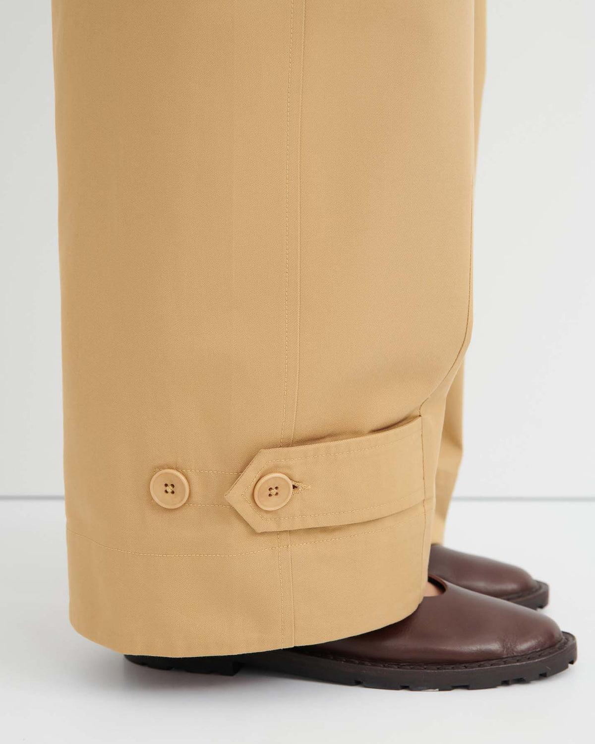 Close-up of the Tab Trouser – Driftwood, wide-leg pants with button details near the hem, featuring a relaxed fit and natural waist, styled over brown shoes on a white background.