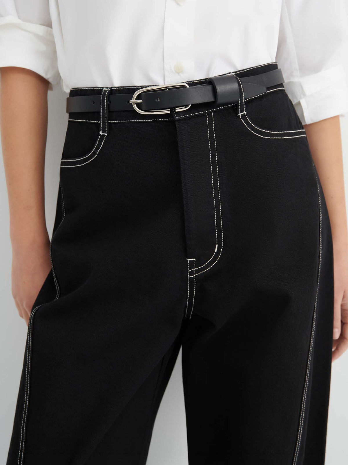 Person wearing a white shirt tucked into Twist Jeans – Black, featuring a high-waisted, relaxed fit design with visible white stitching and styled with a black belt with a silver buckle.