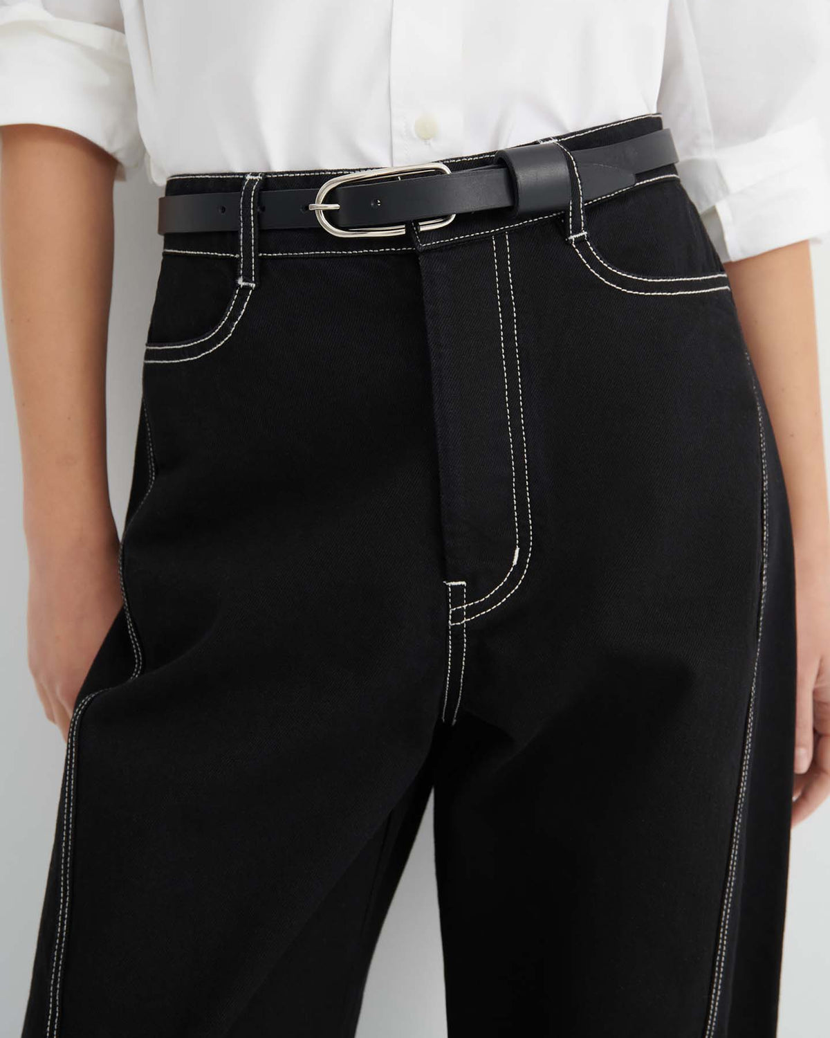 Person wearing a white shirt tucked into Twist Jeans – Black, featuring a high-waisted, relaxed fit design with visible white stitching and styled with a black belt with a silver buckle.