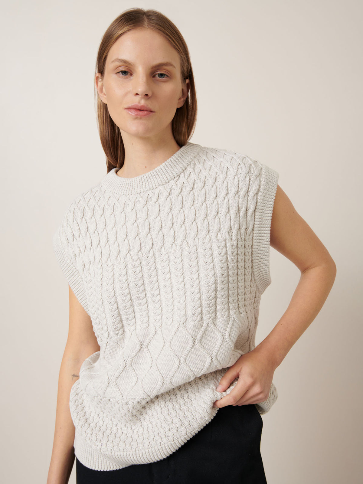 Person wearing the Aran Vest in Oat Melange by Kowtow, showcasing a relaxed fit while posing comfortably against a plain background.