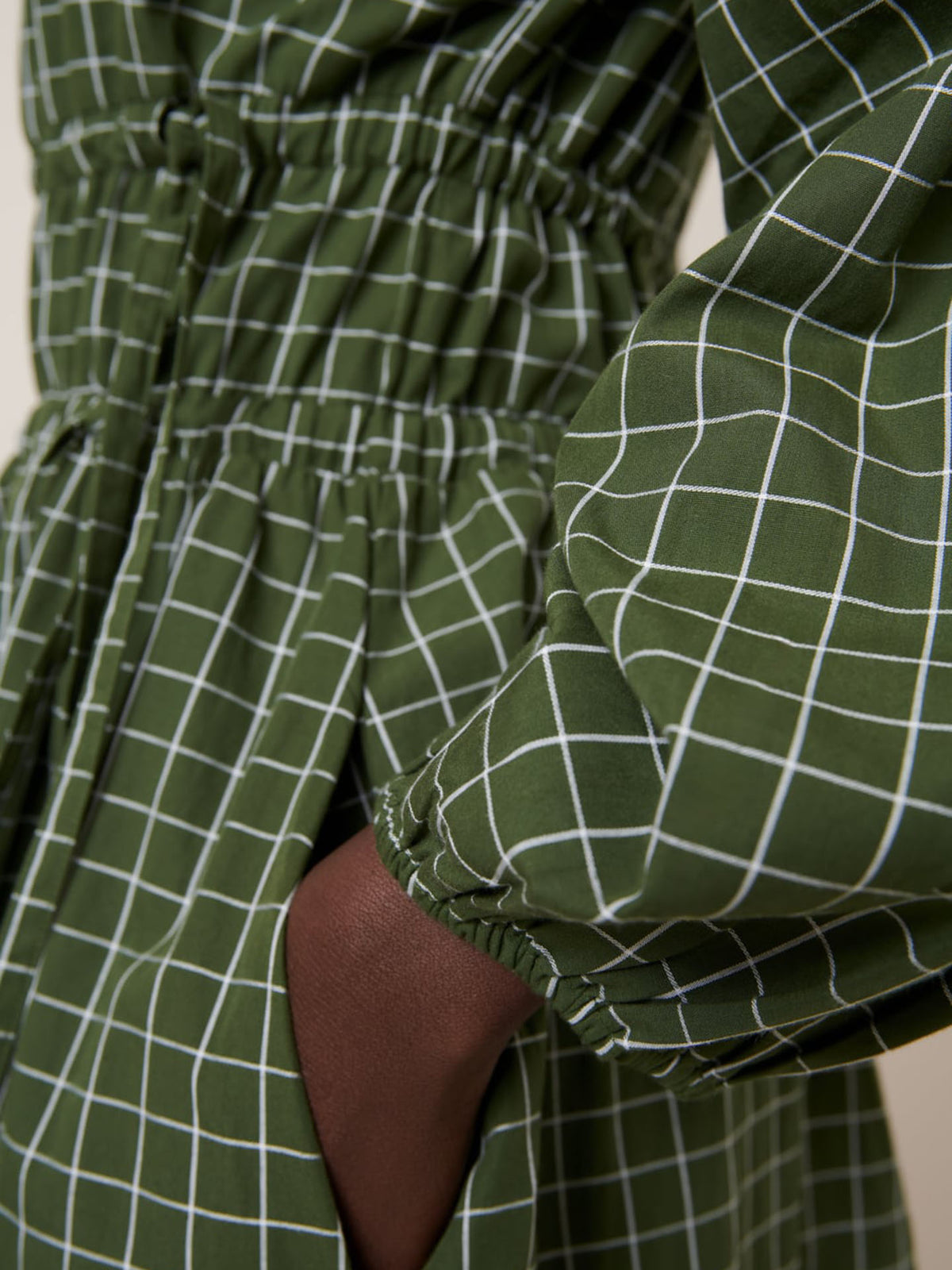 Close-up of a hand in the pocket of the Kowtow Aspen Dress – Forest Grid, featuring a white grid pattern and gathered waist and sleeves for a relaxed fit. Check our size guide for detailed measurements.