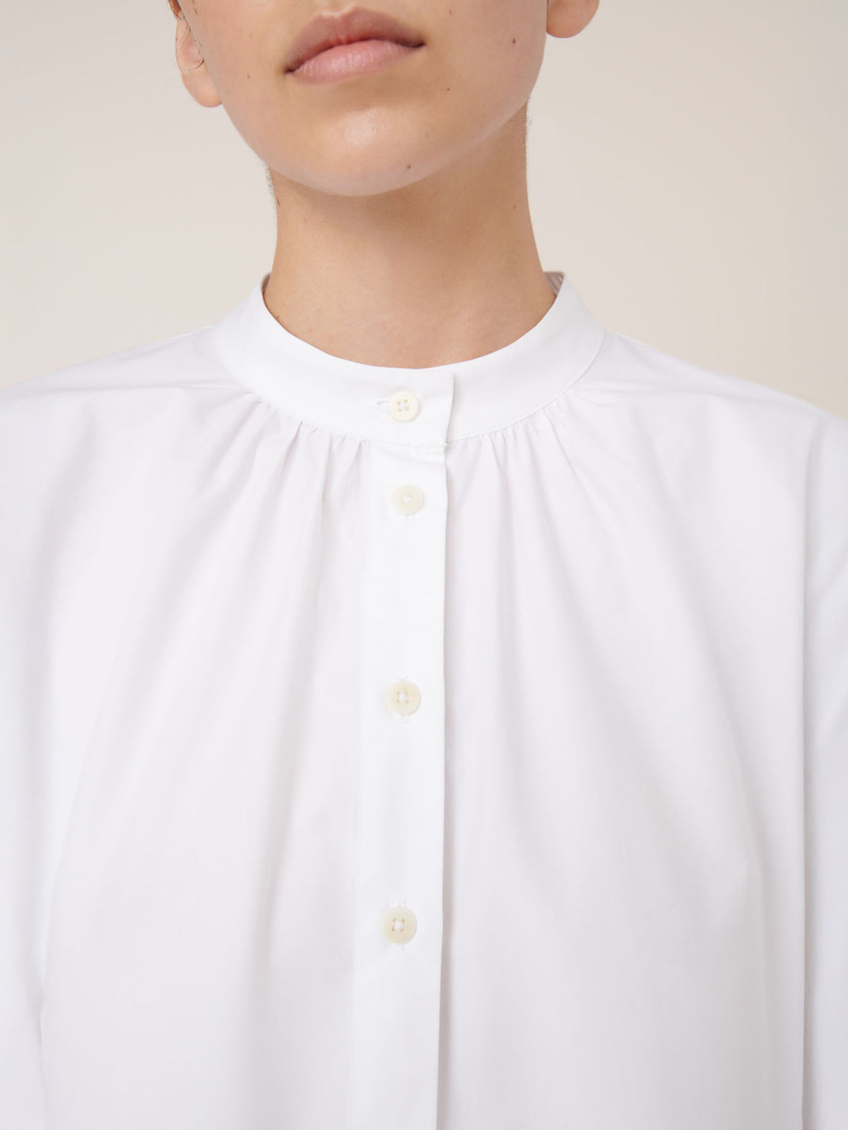 A person wears the Kowtow Atelier Shirt in white, featuring a round collar and boxy fit, photographed from the shoulders up against a plain background.