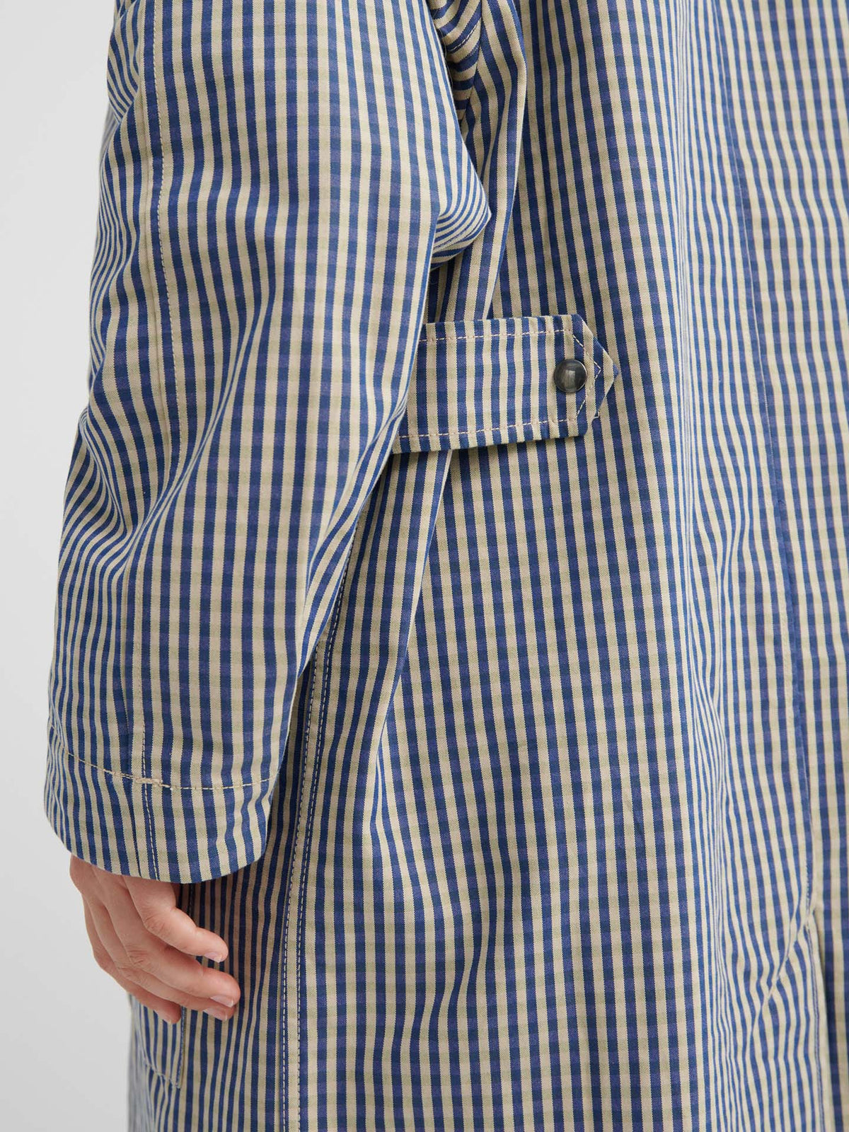 Close-up of a person wearing the Atelier Trench – Landscape Check, highlighting adjustable snap tabs, a buttoned side strap, and detailed sleeves.