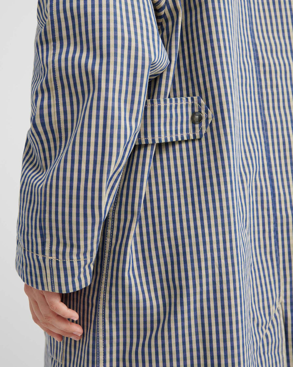 Close-up of a person wearing the Atelier Trench – Landscape Check, highlighting adjustable snap tabs, a buttoned side strap, and detailed sleeves.
