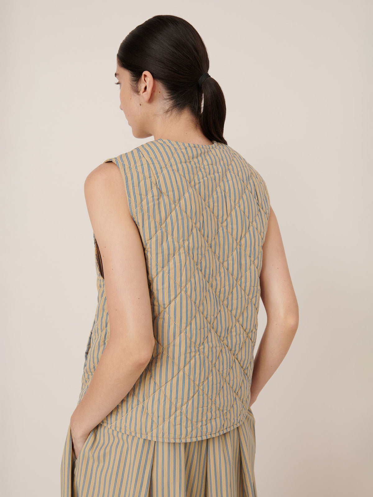 A person with dark hair in a low ponytail models the Kowtow Axis Vest – Double Pinstripe and matching pants from the back against a plain background. The standard fit provides comfort and stays true to size.
