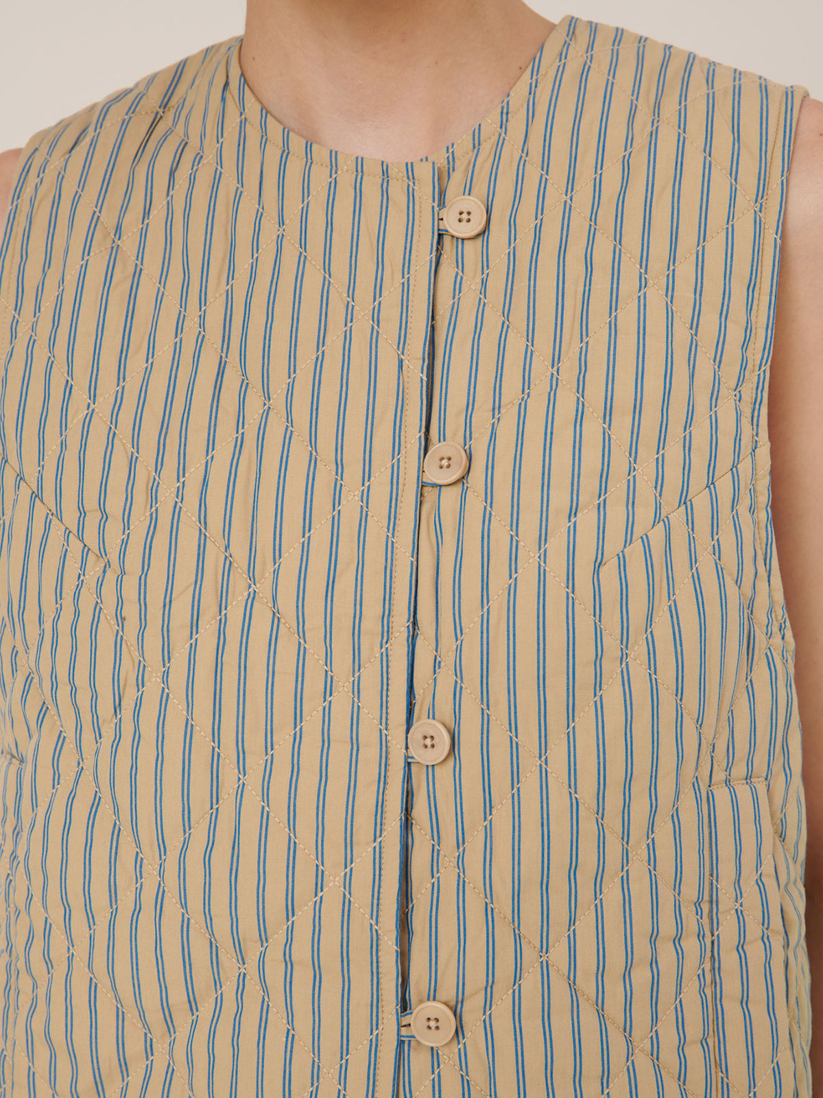 Close-up of the Kowtow Axis Vest – Double Pinstripe: a sleeveless beige vest with vertical blue stripes and four wooden front buttons; garment measurements ensure a standard, true-to-size fit.