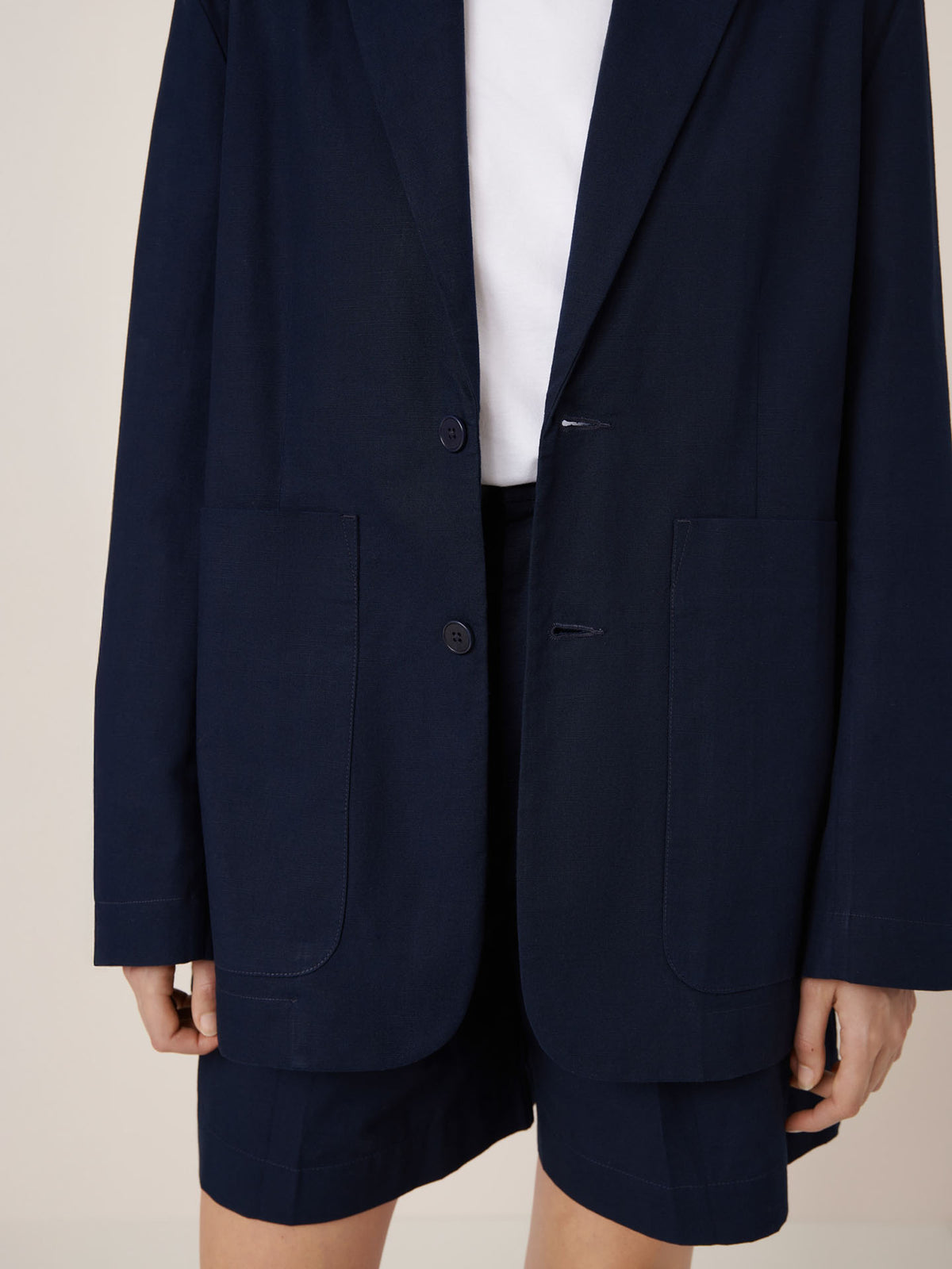 Model wears the Kowtow Carter Blazer in Evening Navy, featuring an oversized fit and large front pockets, paired with matching shorts and a white top. Check our size guide and garment measurements for the perfect fit.