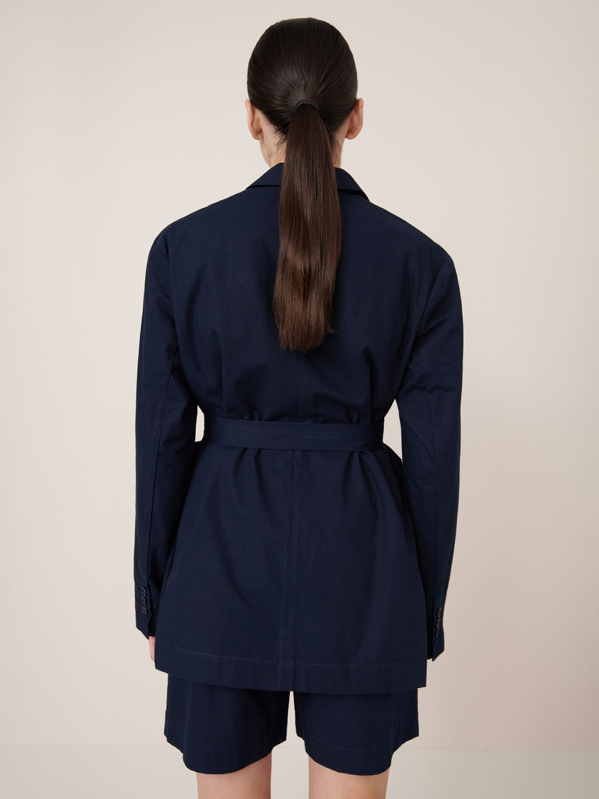 A person with long dark hair in a low ponytail wears the Kowtow Carter Blazer – Evening Navy, featuring an oversized fit and matching shorts, facing away from the camera against a plain background. Check our size guide for measurements.