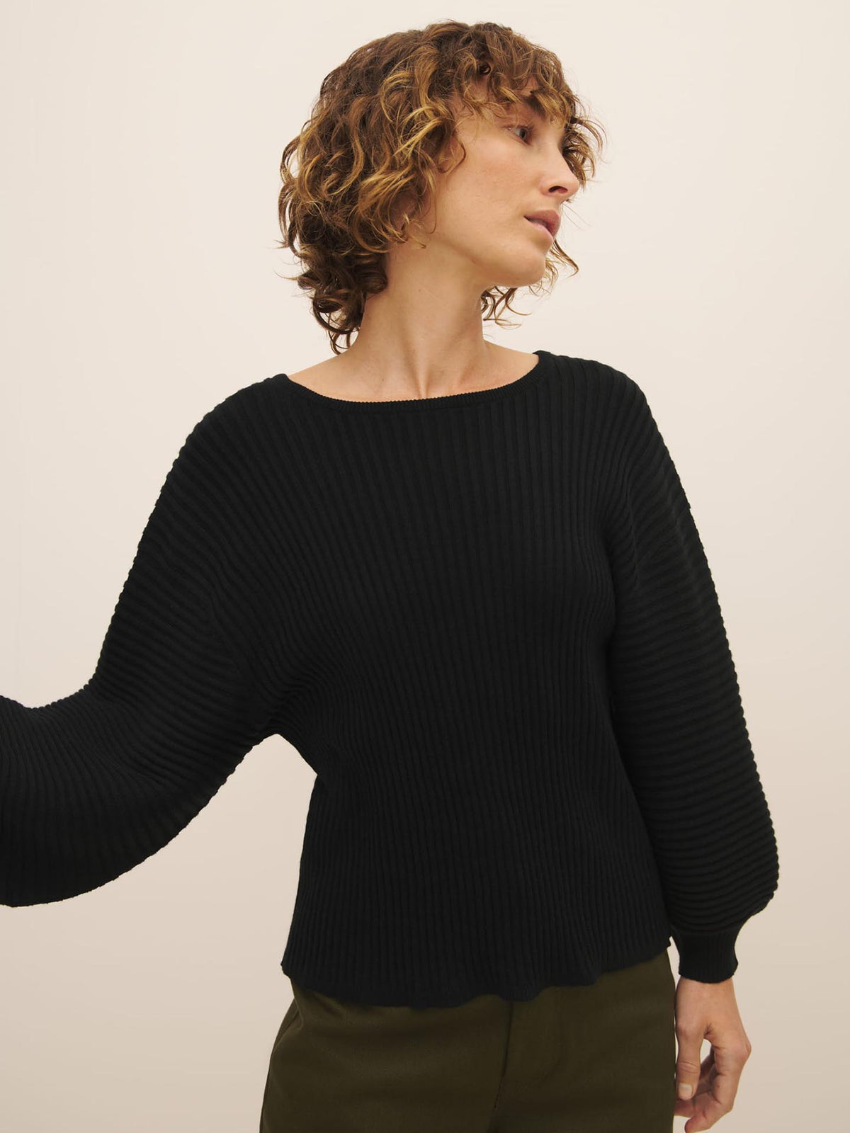Woman in a black Cassia Sweater – Black made from Fairtrade organic cotton, looking to the side against a neutral background by Kowtow.