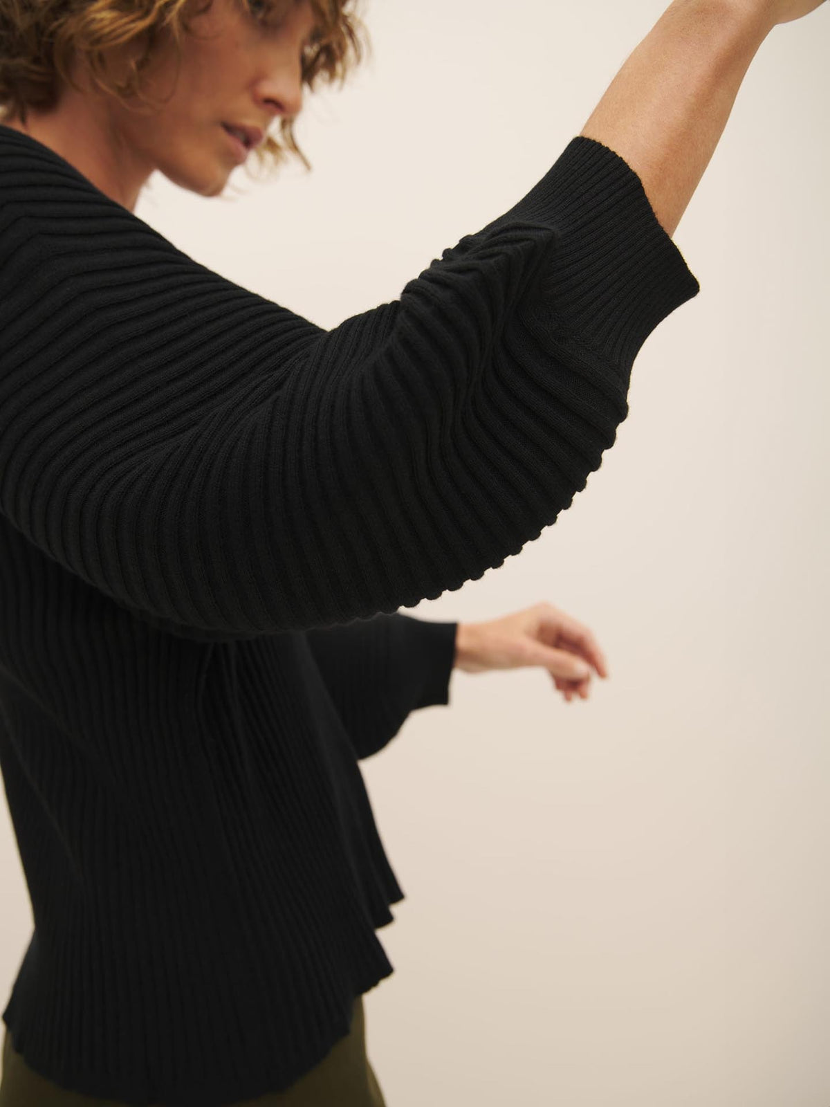 A person in a Kowtow Cassia Sweater – Black extending their arm to the side.