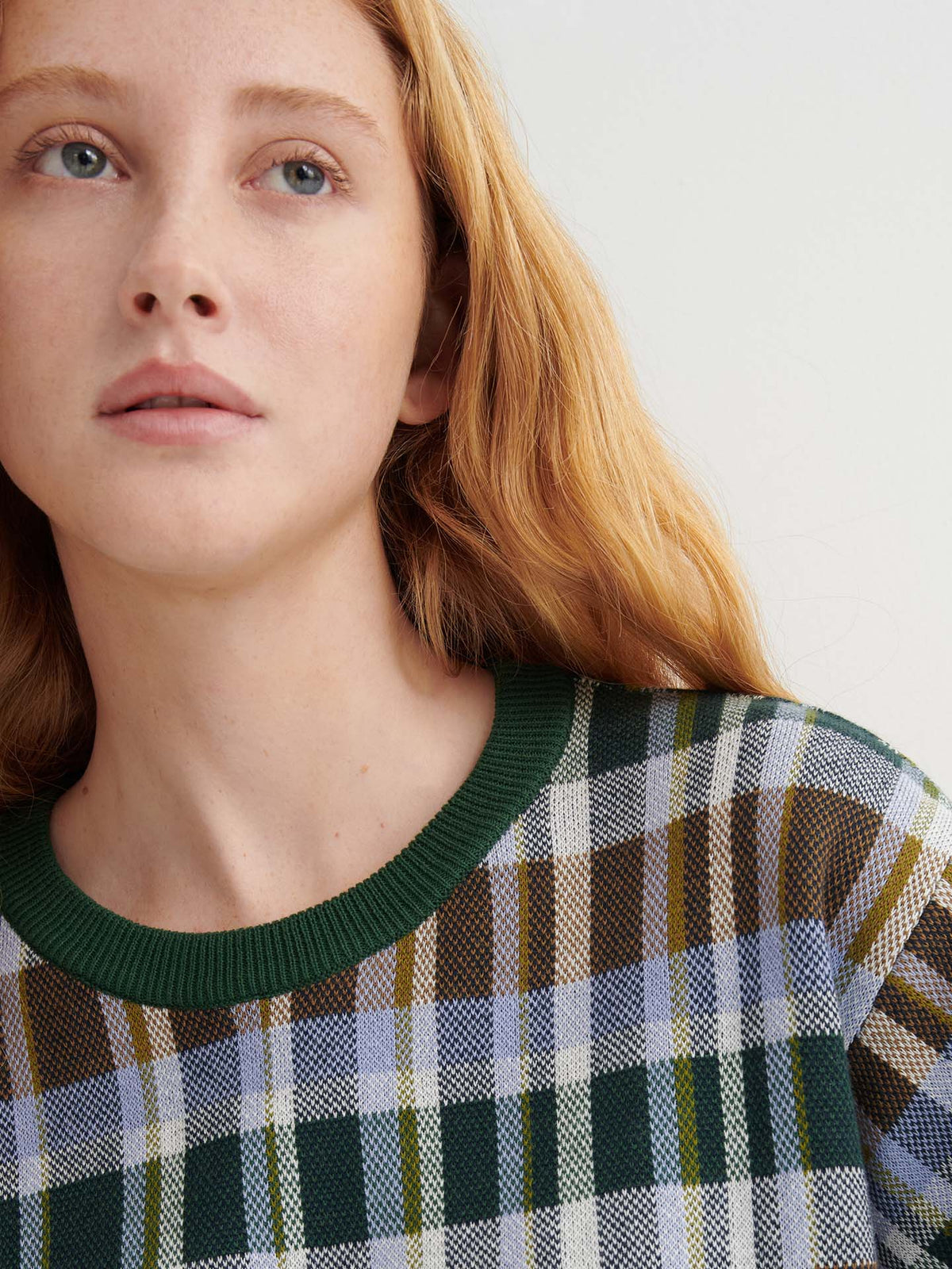 A person with long light brown hair wears the Chequered Tee – Forest with drop shoulder sleeves and looks slightly upward against a light background.