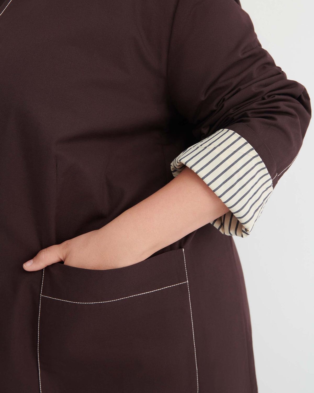 A person wearing a dark brown long-sleeve shirt with striped cuffs has their hand in a front pocket.
