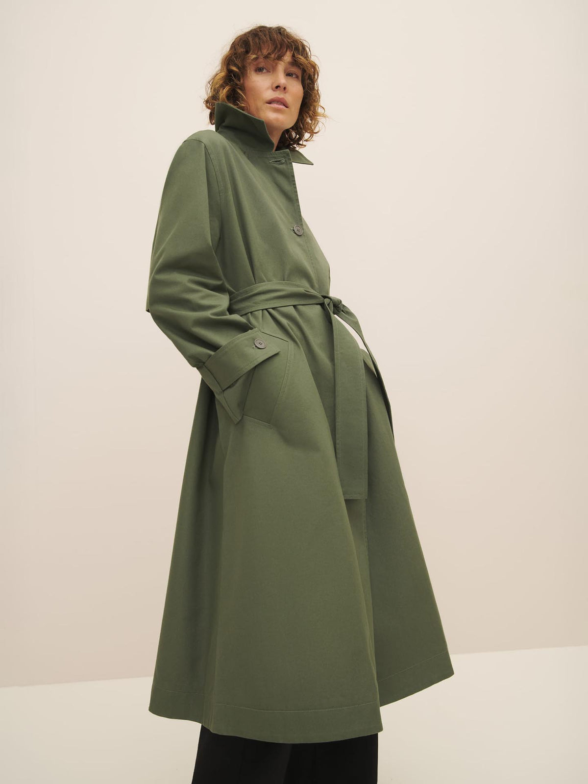 Woman modeling a Cleo trench coat in sage with a belt, designed for a relaxed fit by Kowtow.