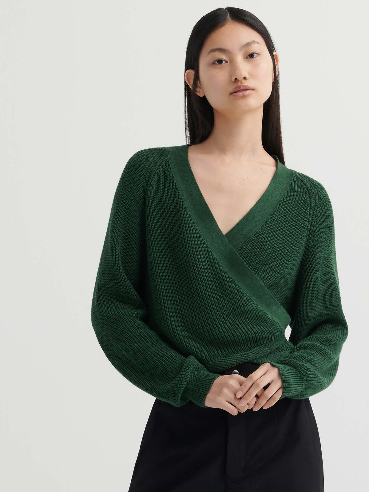 A person with long straight hair wears the Composure Cardigan – Forest in a relaxed fit with black pants, standing against a plain light background.