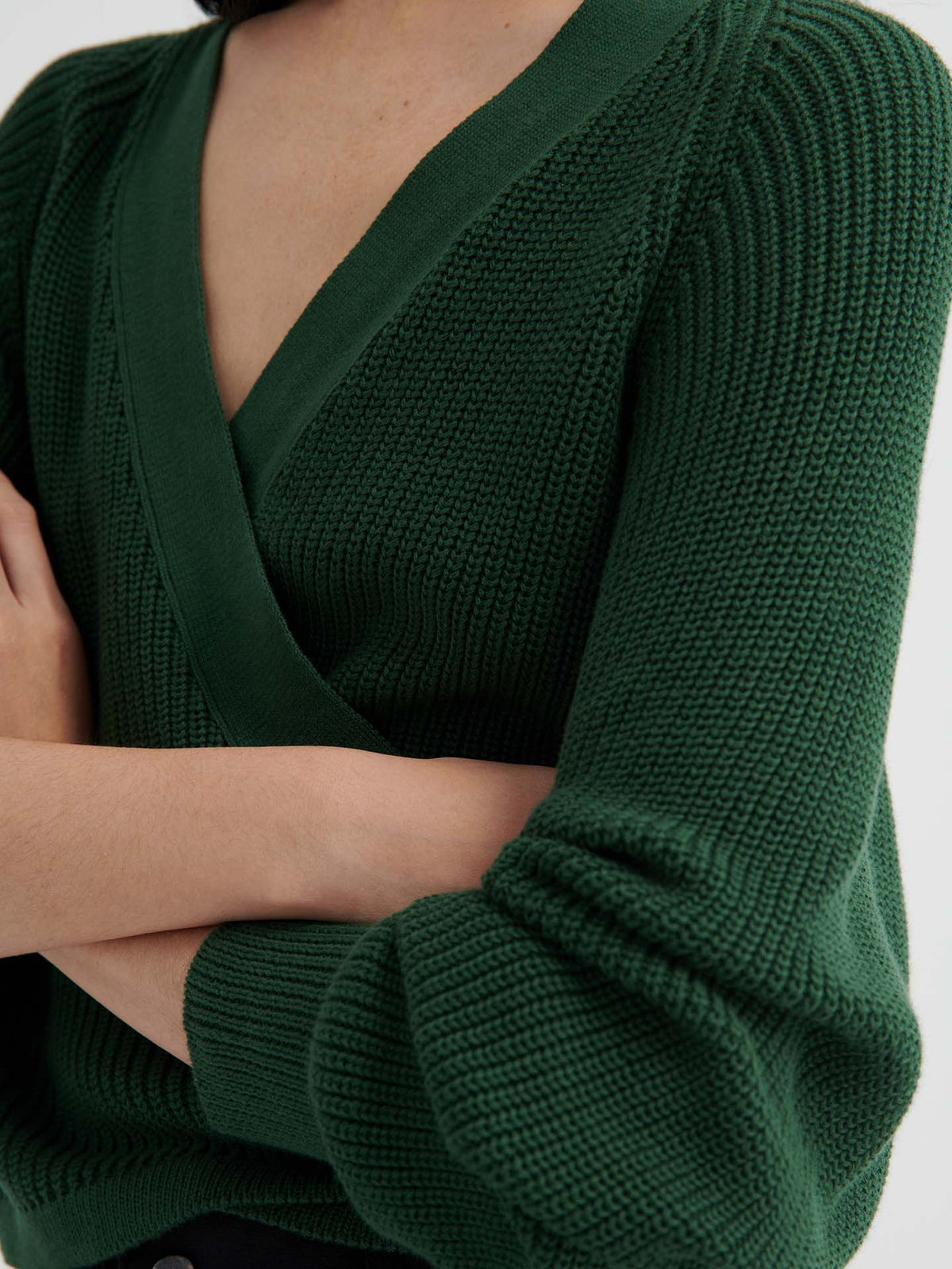 A person models the Composure Cardigan – Forest, featuring a deep green ribbed knit, crossover V-neck, and long sleeves with a relaxed fit. See our sizing guide to find your perfect match.