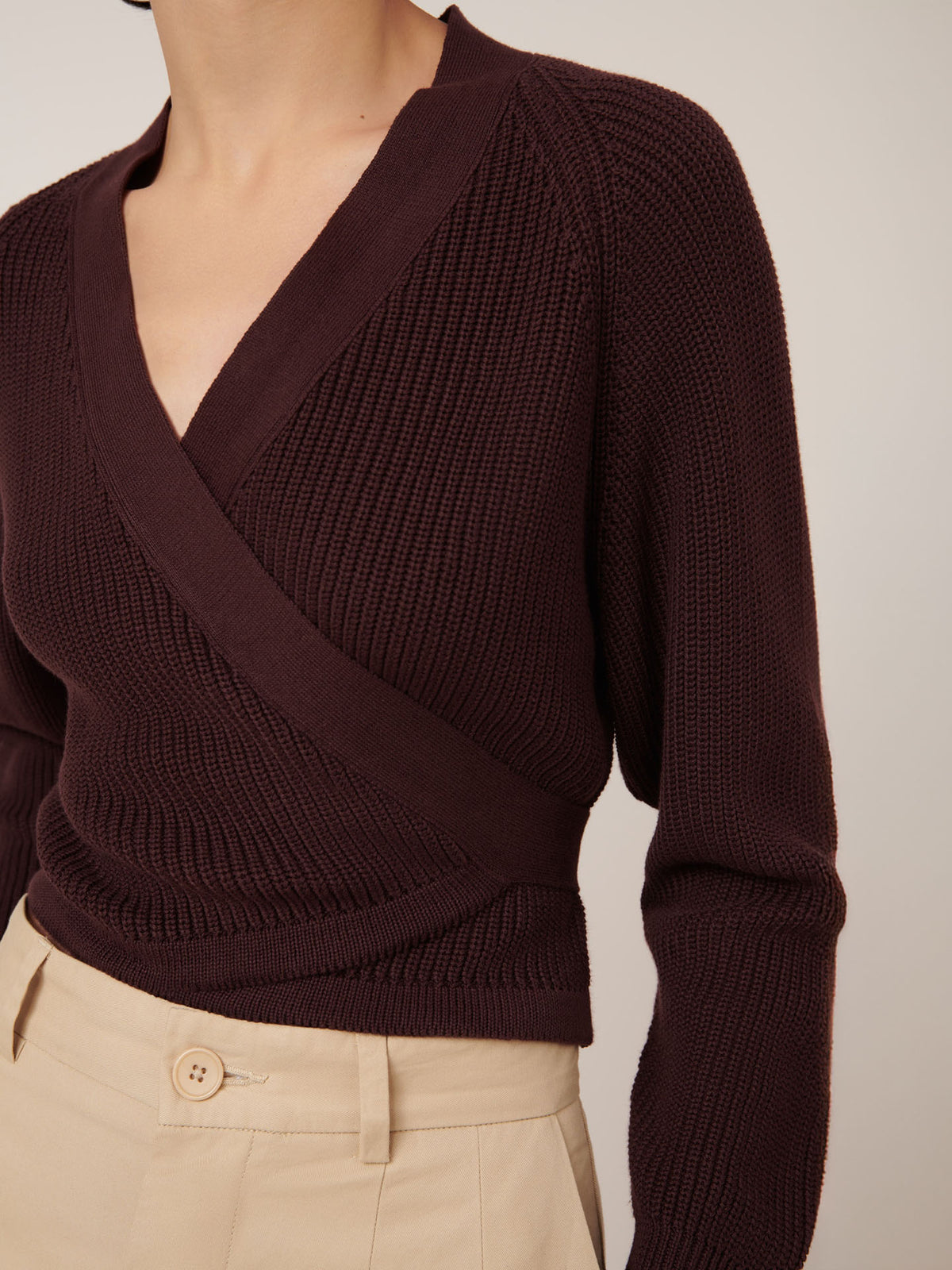 A person is wearing the Kowtow Composure Cardigan in Mahogany styled with high-waisted beige trousers featuring button details, showcasing a standard fit.