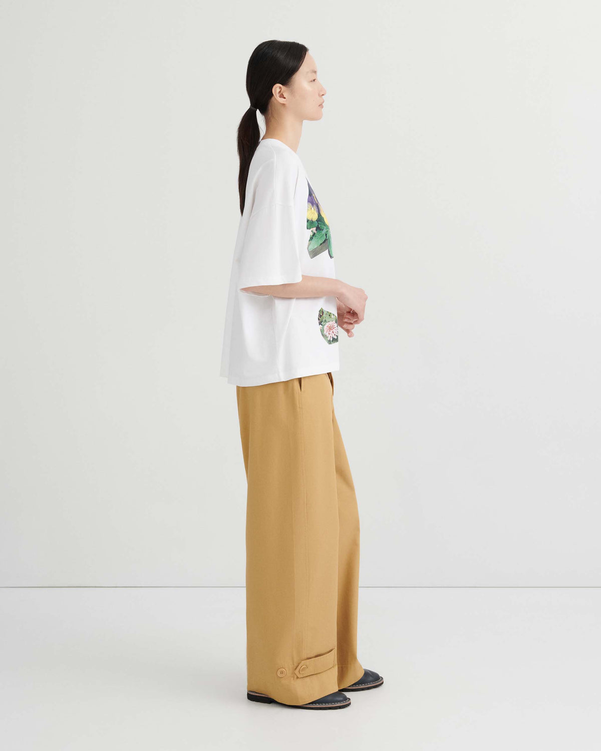 A person wearing a white graphic t-shirt and loose tan trousers standing in profile.