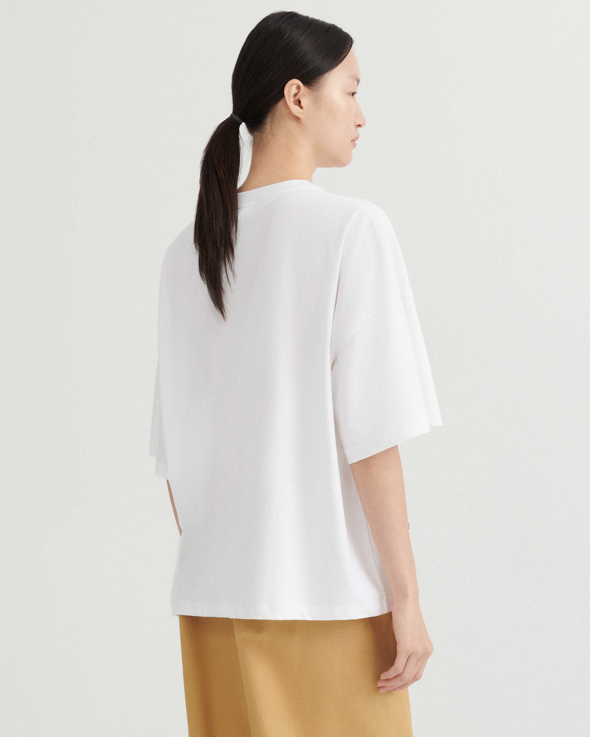 A person viewed from behind wearing a white, loose-fit t-shirt and tan pants.