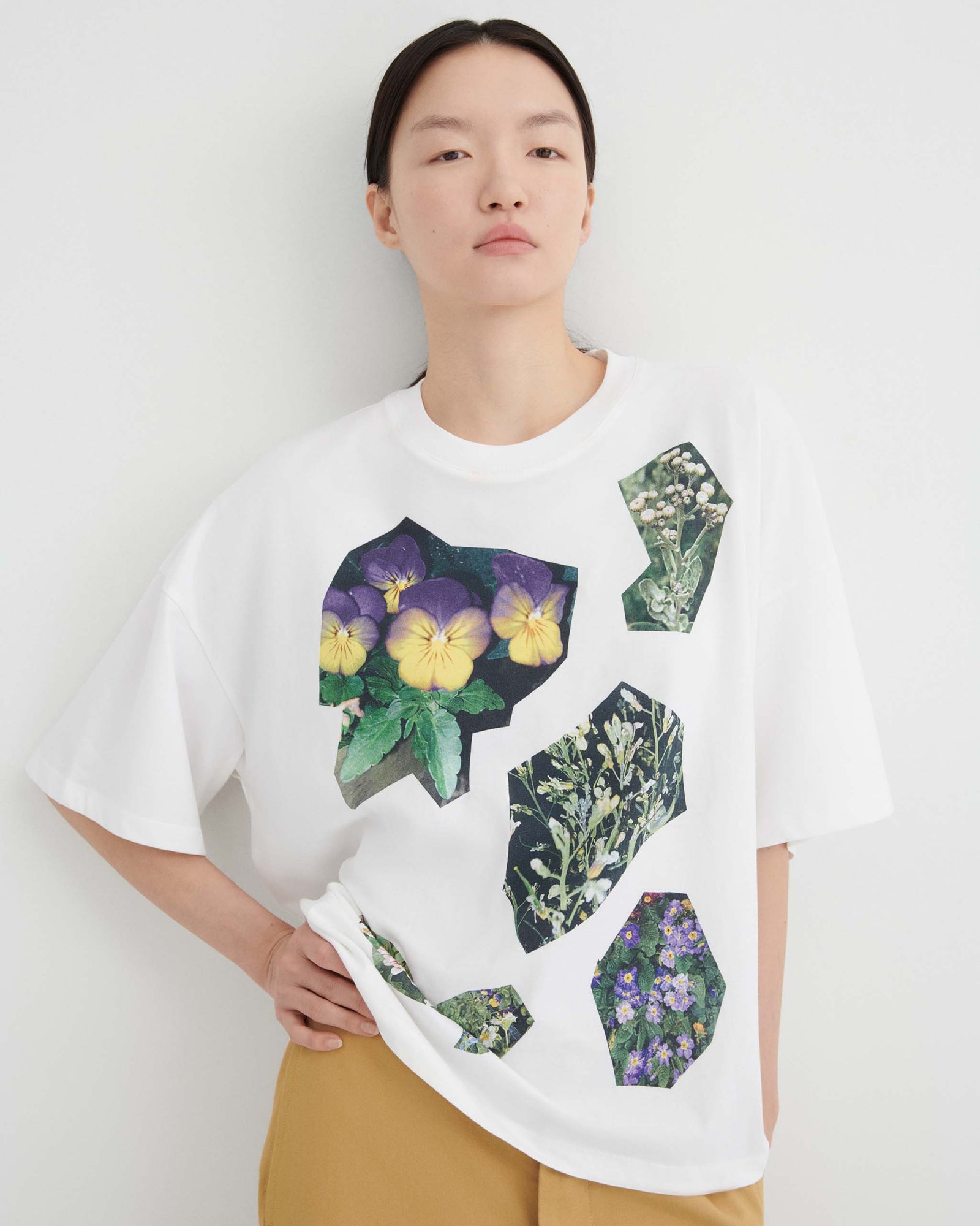A person wearing a white t-shirt featuring a collage of flower and plant illustrations in geometric shapes.