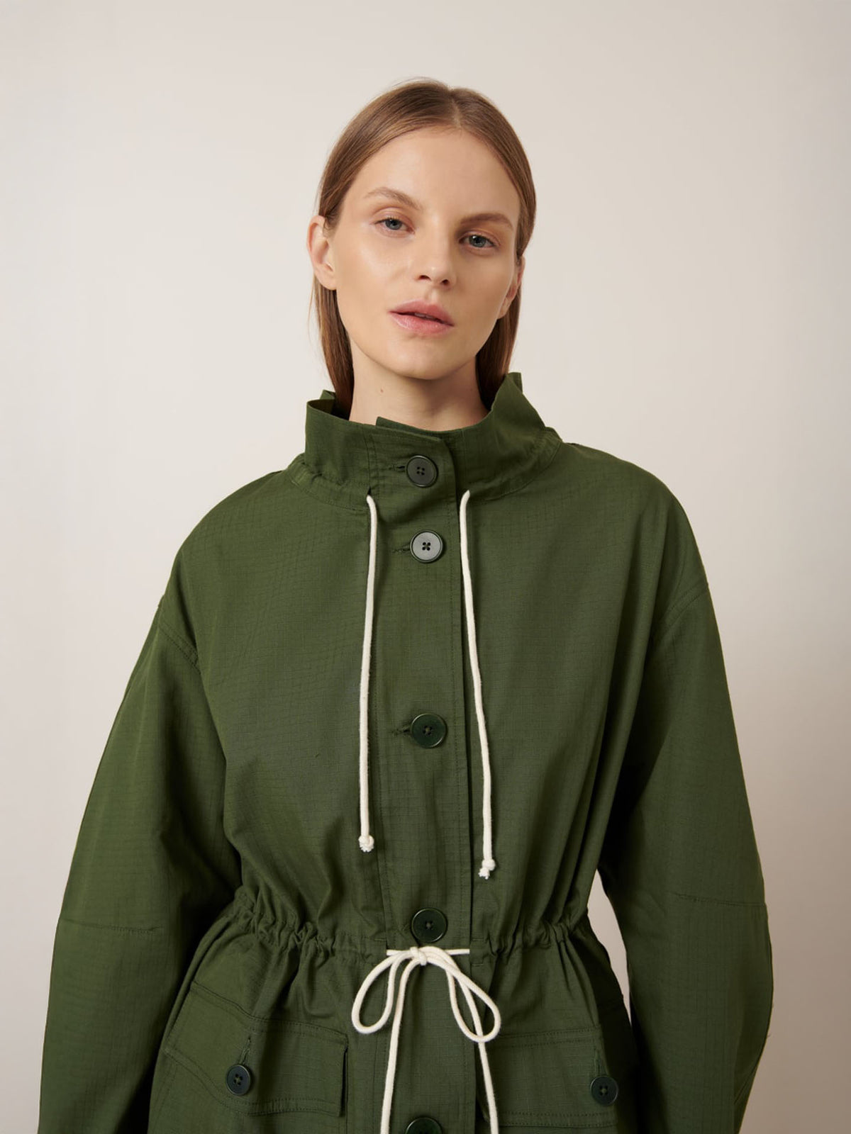 A person wears the Kowtow Echo Jacket – Forest, an oversized green button-up with white drawstrings, standing against a plain light background.
