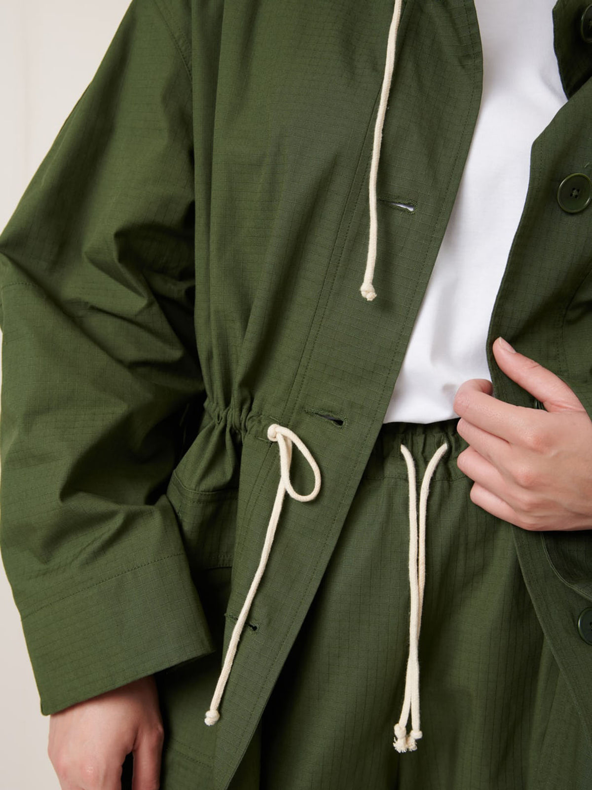 A person wears the Echo Jacket – Forest by Kowtow in an oversized fit with matching pants over a white shirt, shown from shoulders to mid-thigh. Review measurements for details or size down for a more tailored silhouette.