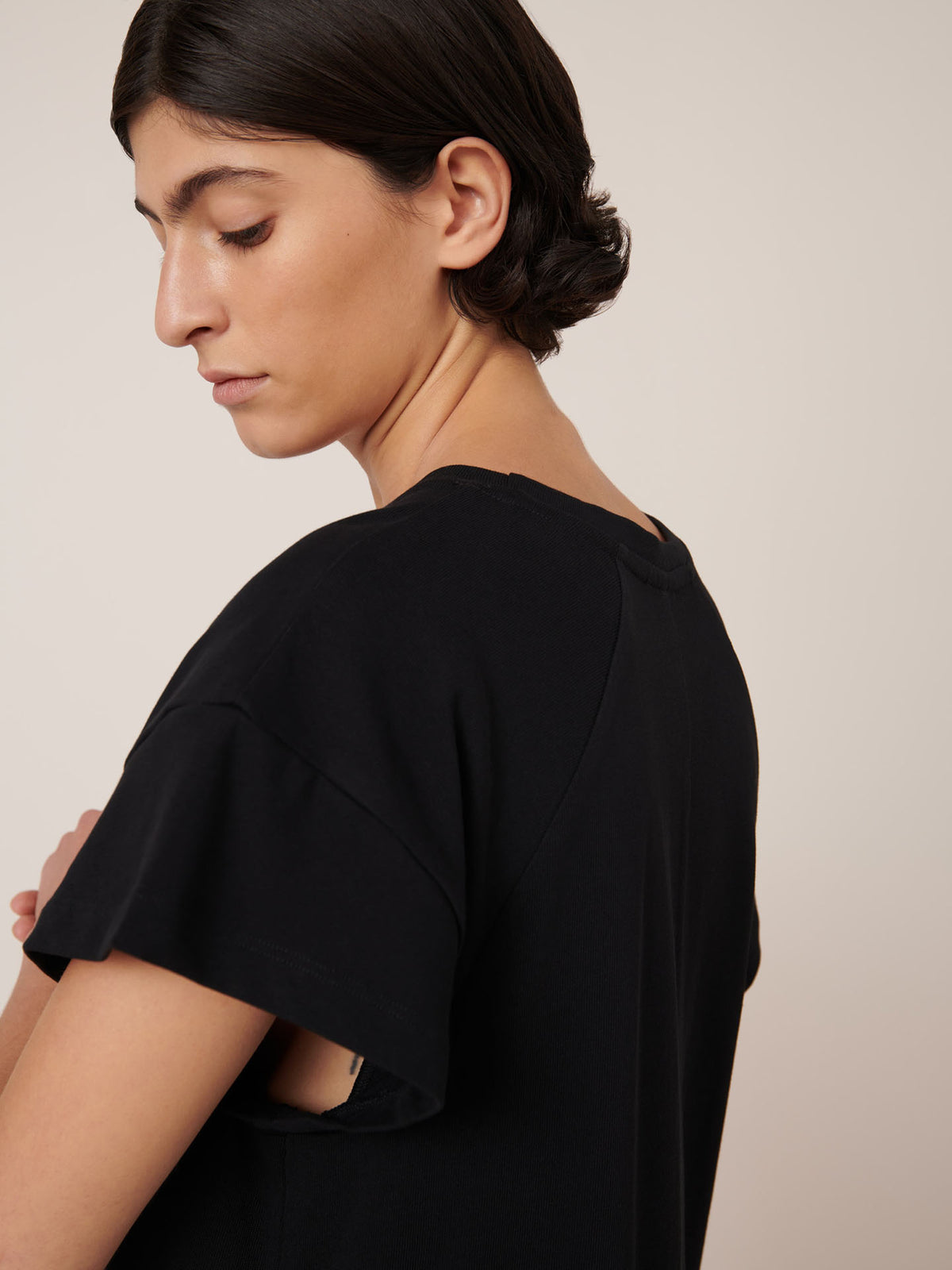 A person with short dark hair wears the Kowtow Effect Dress in black, standing sideways with eyes closed against a neutral background.