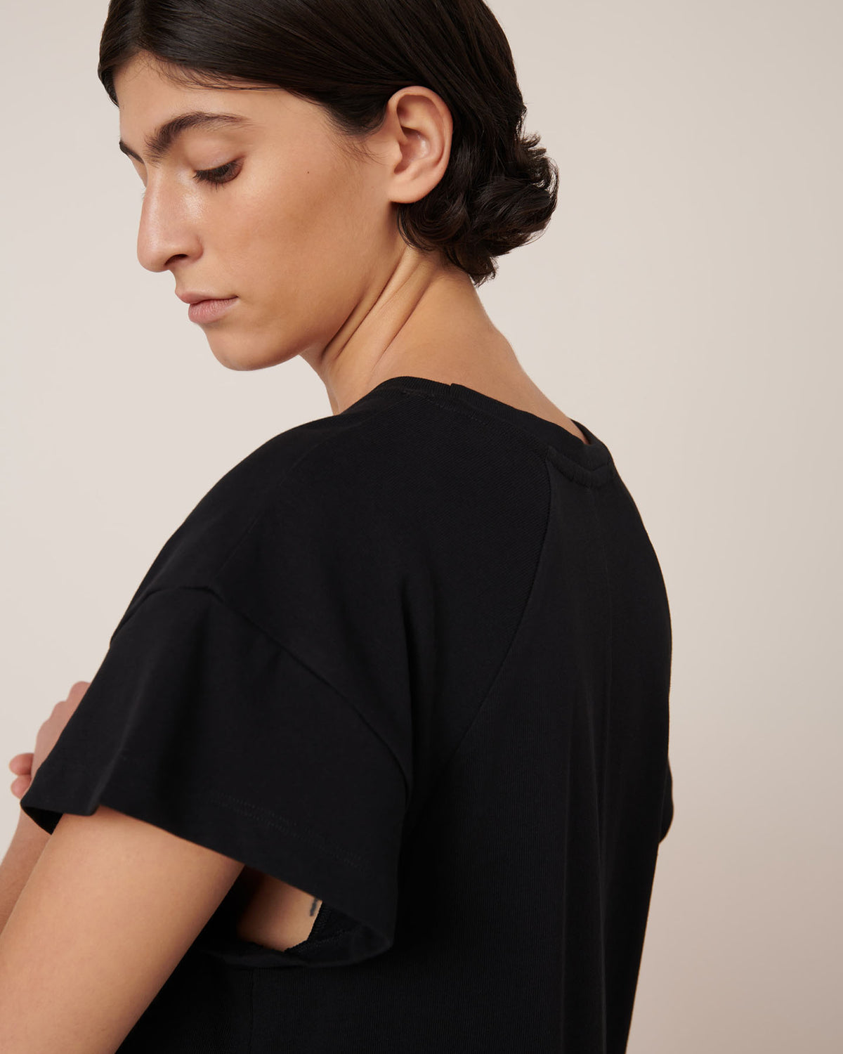 A person with short dark hair wears the Kowtow Effect Dress in black, standing sideways with eyes closed against a neutral background.