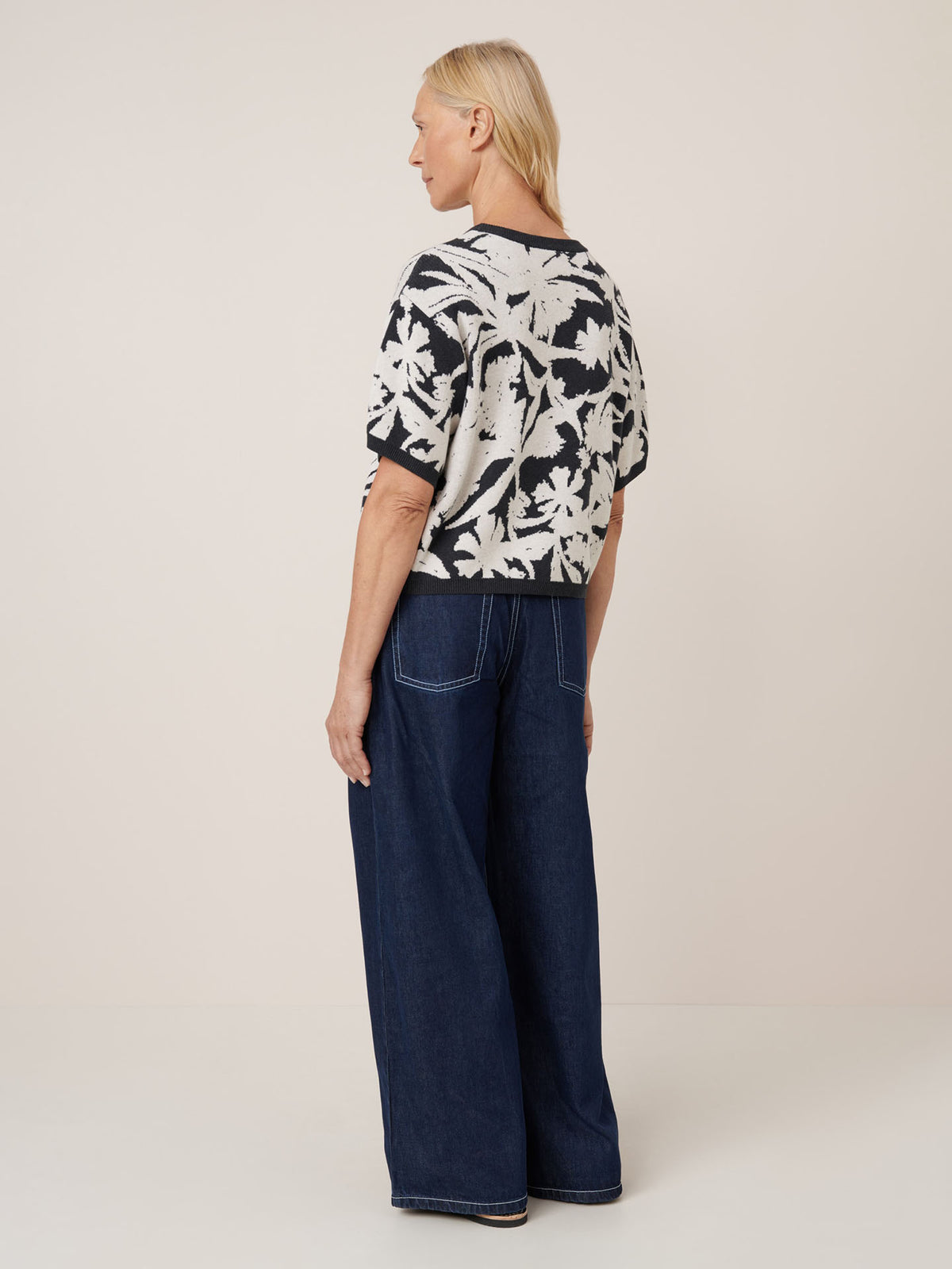 A person with blonde hair, seen from behind, wears the Kowtow Etched Top in etched jacquard and relaxed fit wide-leg dark blue jeans.