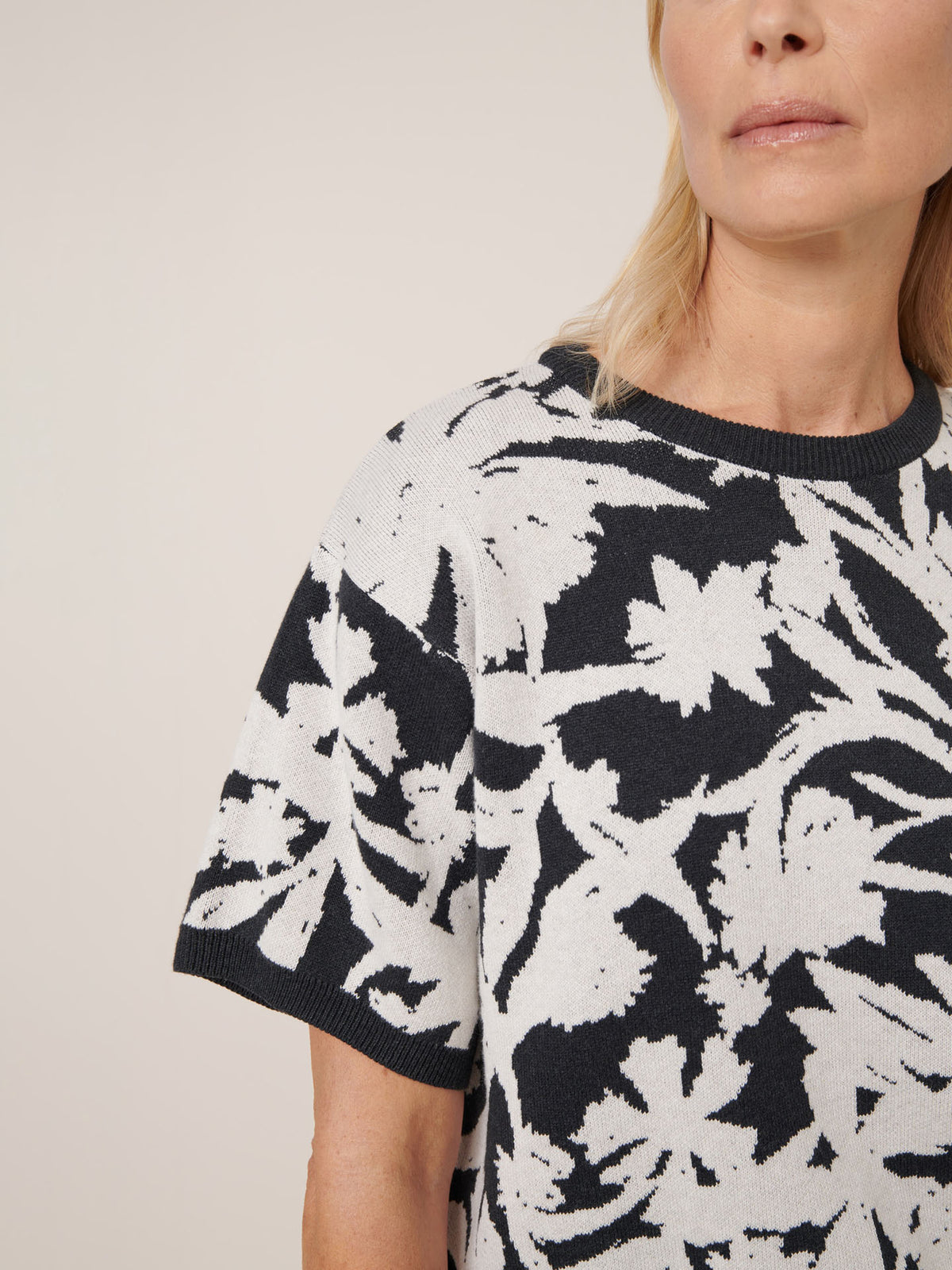 A woman wears the Kowtow Etched Top in Etched Jacquard, a relaxed-fit short-sleeve sweater with a black and white floral pattern, shown from the shoulders up against a plain background.