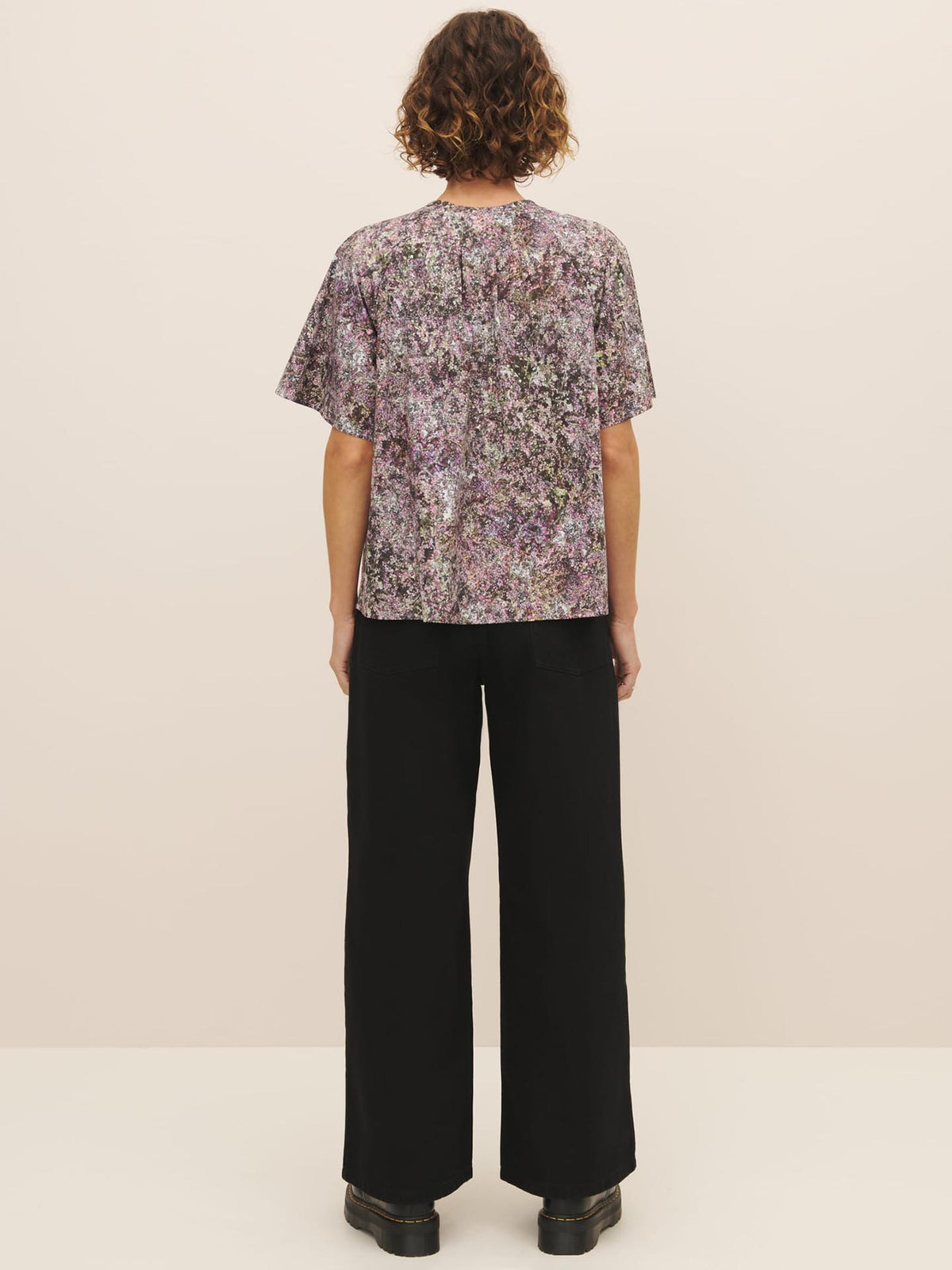 Person standing with their back to the camera, wearing an oversized fit Kowtow Etude Top – Bouquet shirt and black trousers.