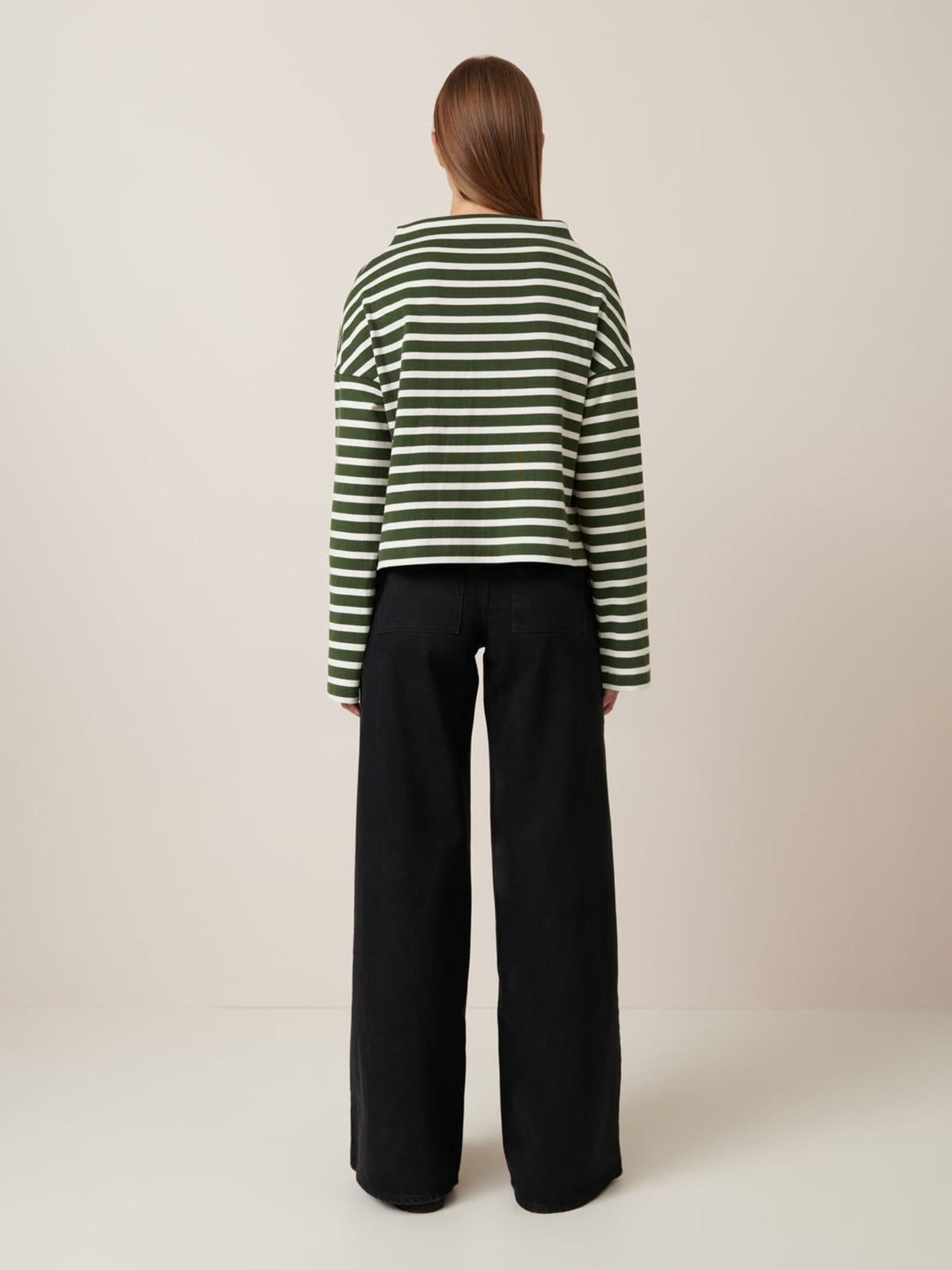 Person stands with back to camera in a neutral room, wearing Kowtow&#39;s Field Top – Green Lily Stripe and loose black pants, showcasing its relaxed fit. Check our size guide for garment measurements.