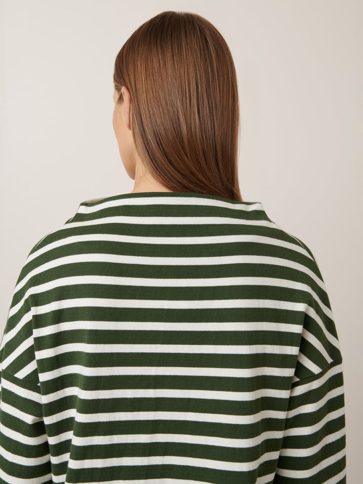 Person with straight brown hair, seen from behind, wears the Kowtow Field Top – Green Lily Stripe (a relaxed fit green and white striped shirt) against a plain light background.