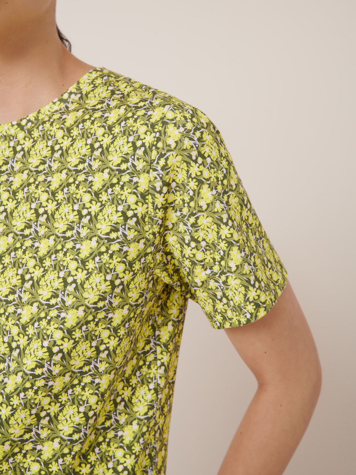 Close-up of a person wearing the Kowtow Flora Tee in a yellow and green floral print, standing against a plain light background. See our size guide for garment measurements and fit details.