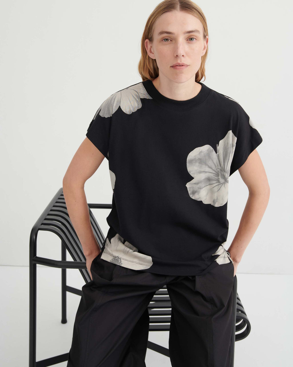 A person wearing a black short-sleeved t-shirt with large, pale grey flower prints, paired with black trousers.