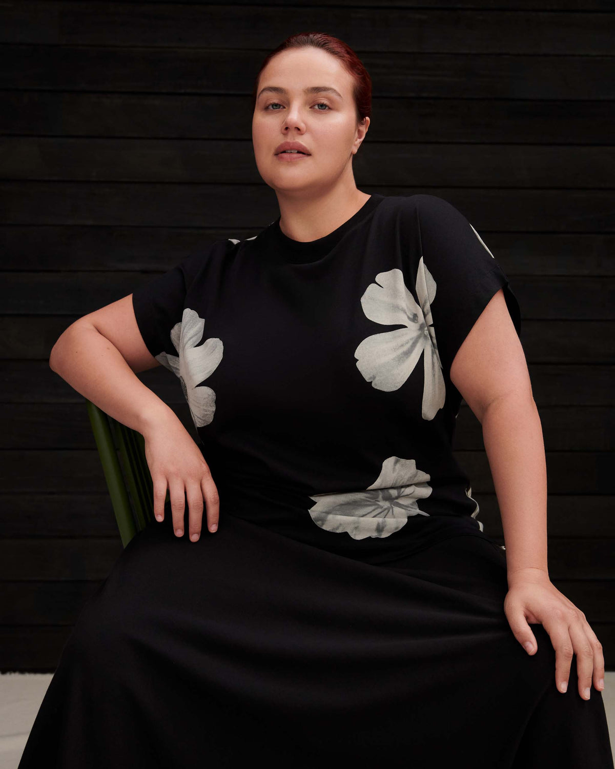 A person wearing a black t-shirt dress with white floral prints sitting on a green chair.