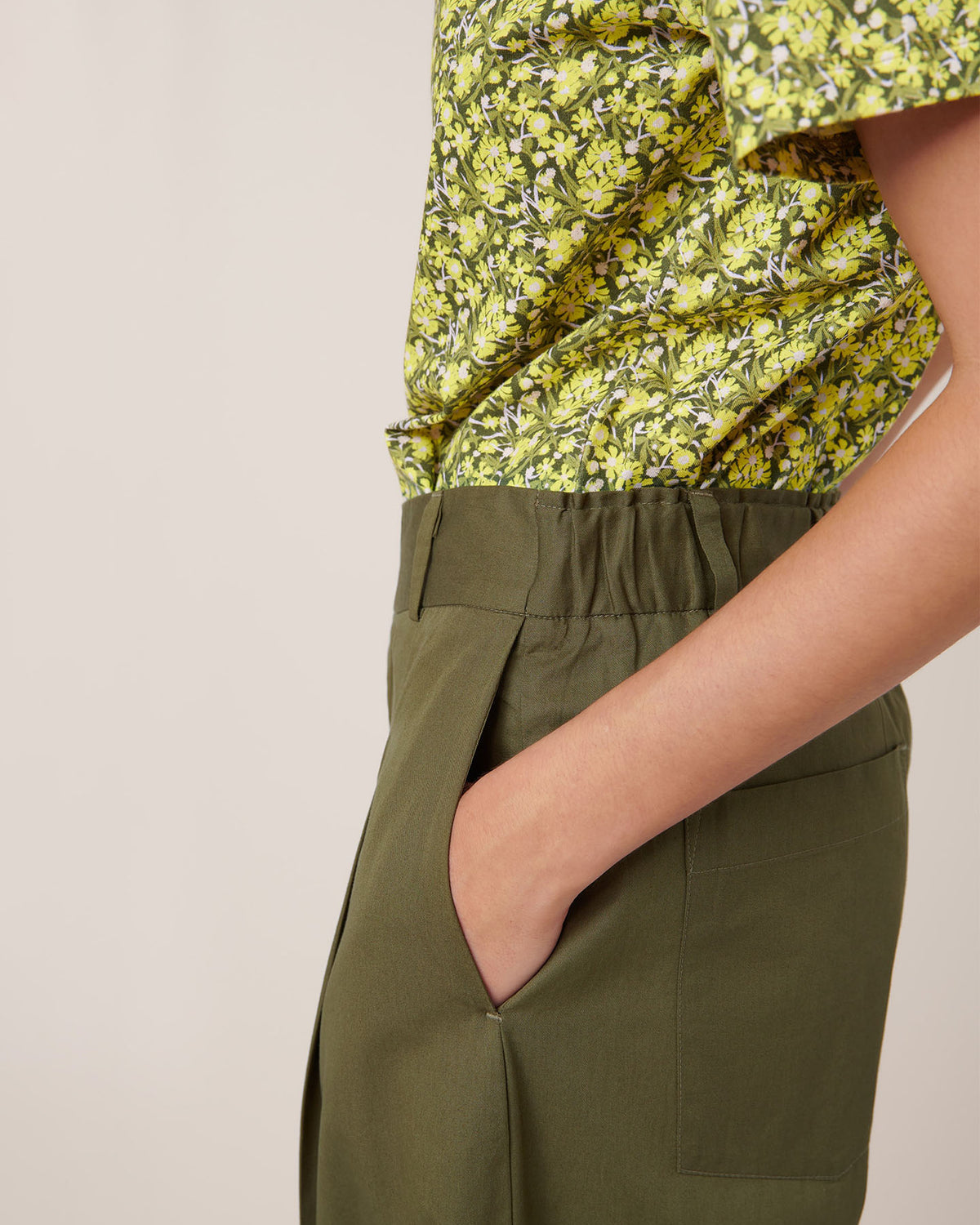A person wears an olive green floral short-sleeve shirt tucked into Kowtow's Harmony Pant – Ivy, relaxed fit and high-waisted, with a hand in the pocket for a casual Kowtow look.