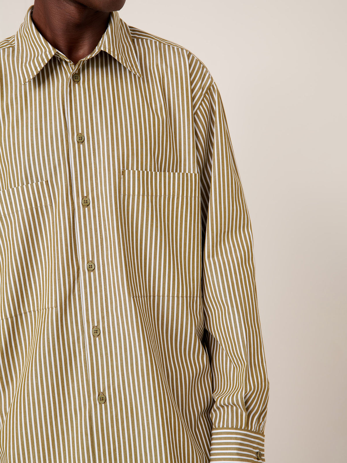 A person wearing the Kowtow Henry Shirt – Treetop Stripe, a relaxed fit long-sleeved shirt with vertical beige and white stripes, stands against a plain background.