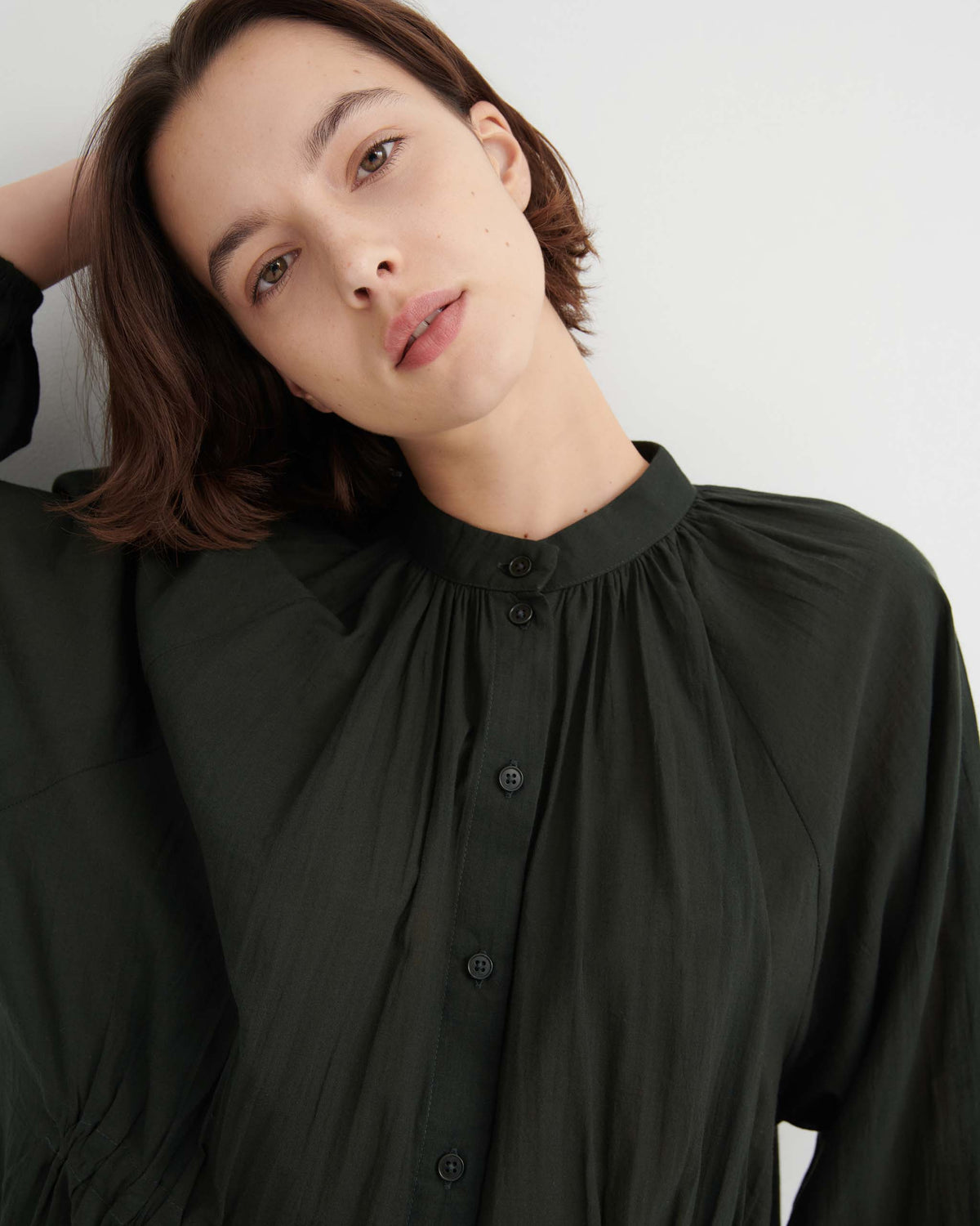 A woman wearing a dark green, long-sleeved button-down blouse with a stand collar.