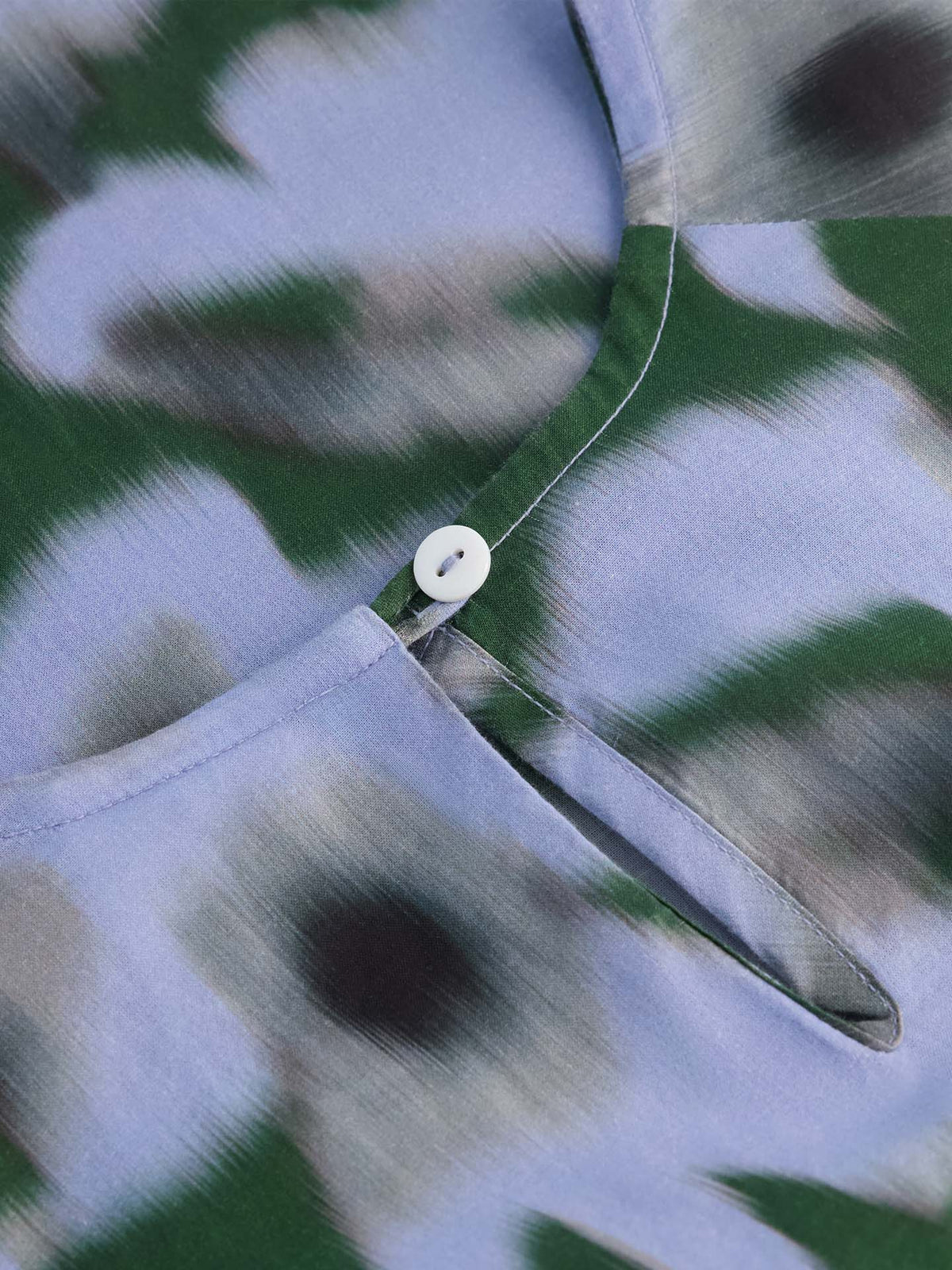 Close-up of the Illustrate Dress – Misty Floral by Kowtow, featuring a green, black, and light blue abstract floral pattern with a small white button at the neckline and a standard fit.