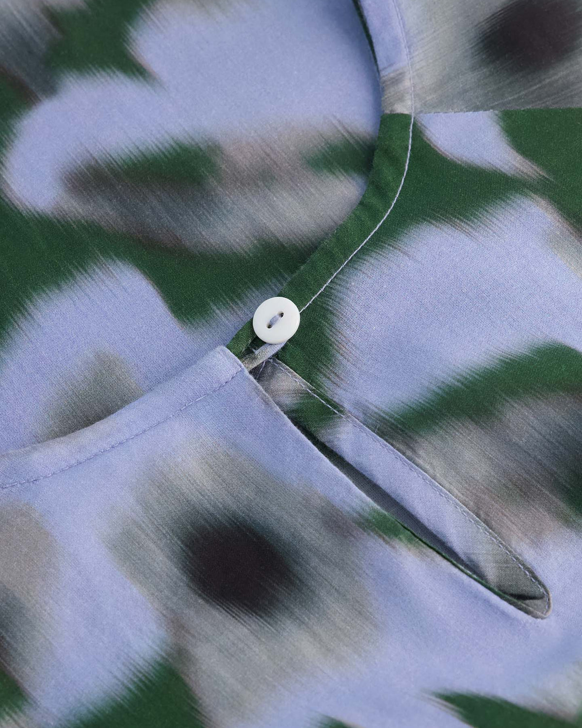 Close-up of the Illustrate Dress – Misty Floral by Kowtow, featuring a green, black, and light blue abstract floral pattern with a small white button at the neckline and a standard fit.