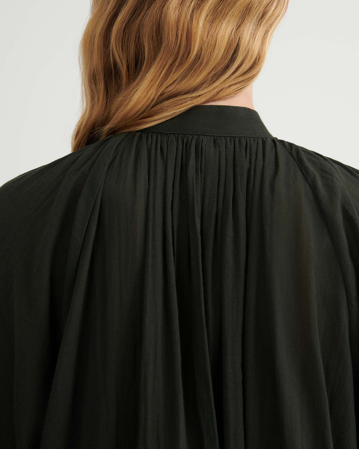 Back view of a dark green collared shirt with gathered detailing at the yoke.