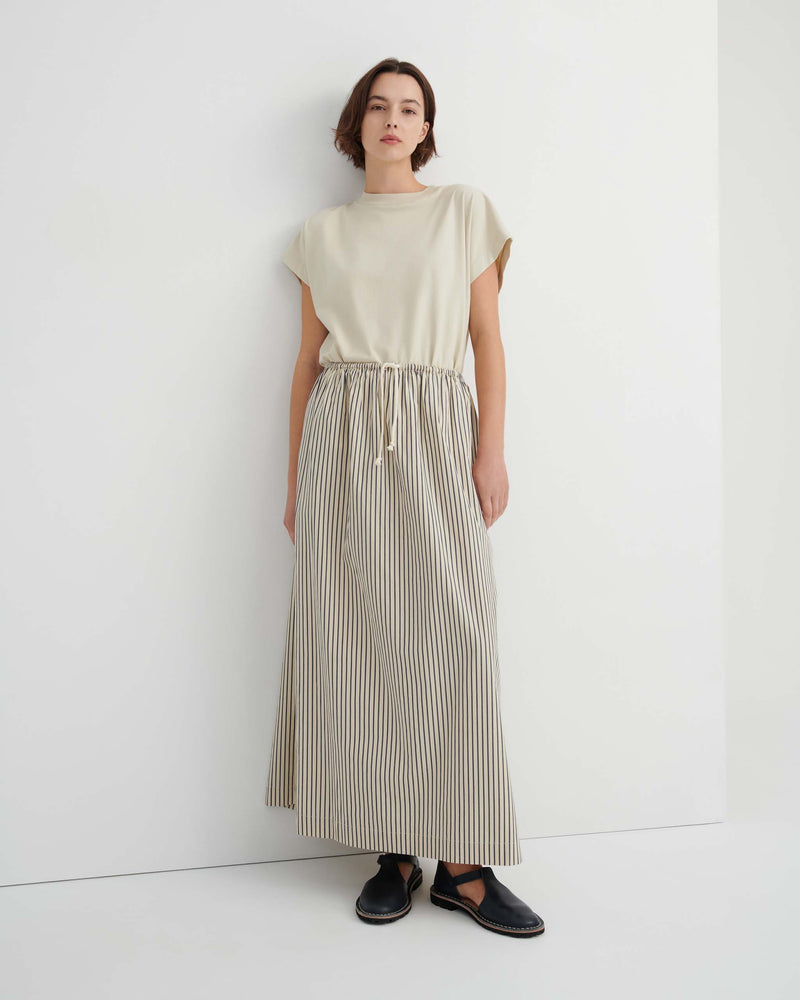 A person wearing a beige short-sleeved top and a floor-length, striped drawstring skirt with black sandals.