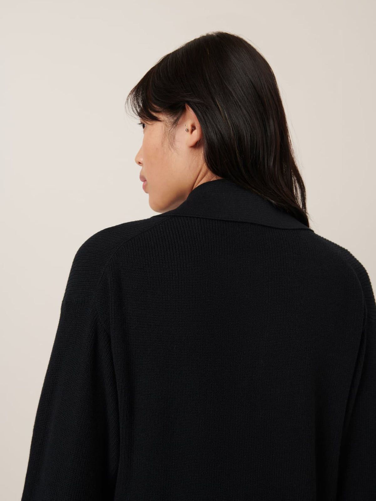 A person with long black hair is seen from behind, donning a Kowtow standard-fit Merel Cardigan in black against a neutral background.